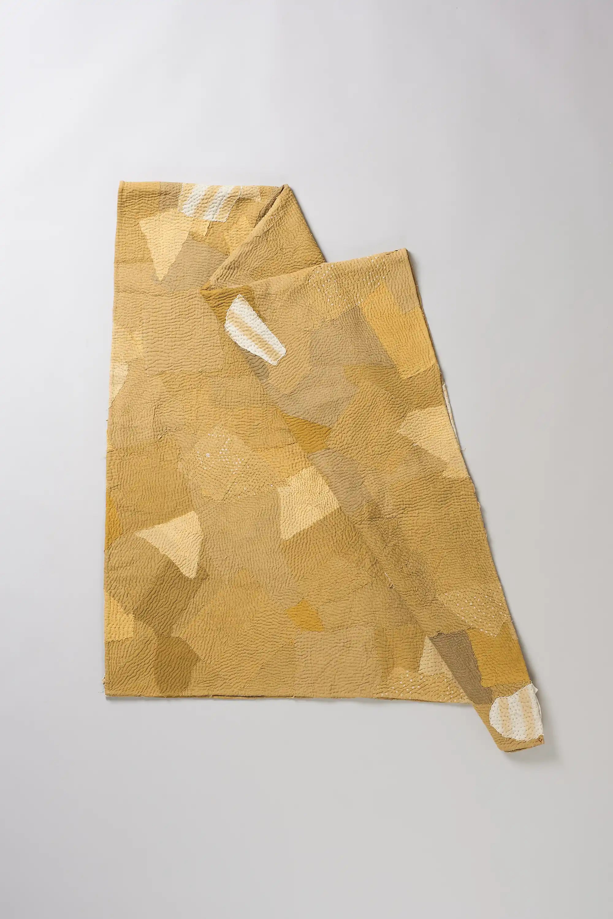 Patchwork quilt in shades of yellow on a light grey background