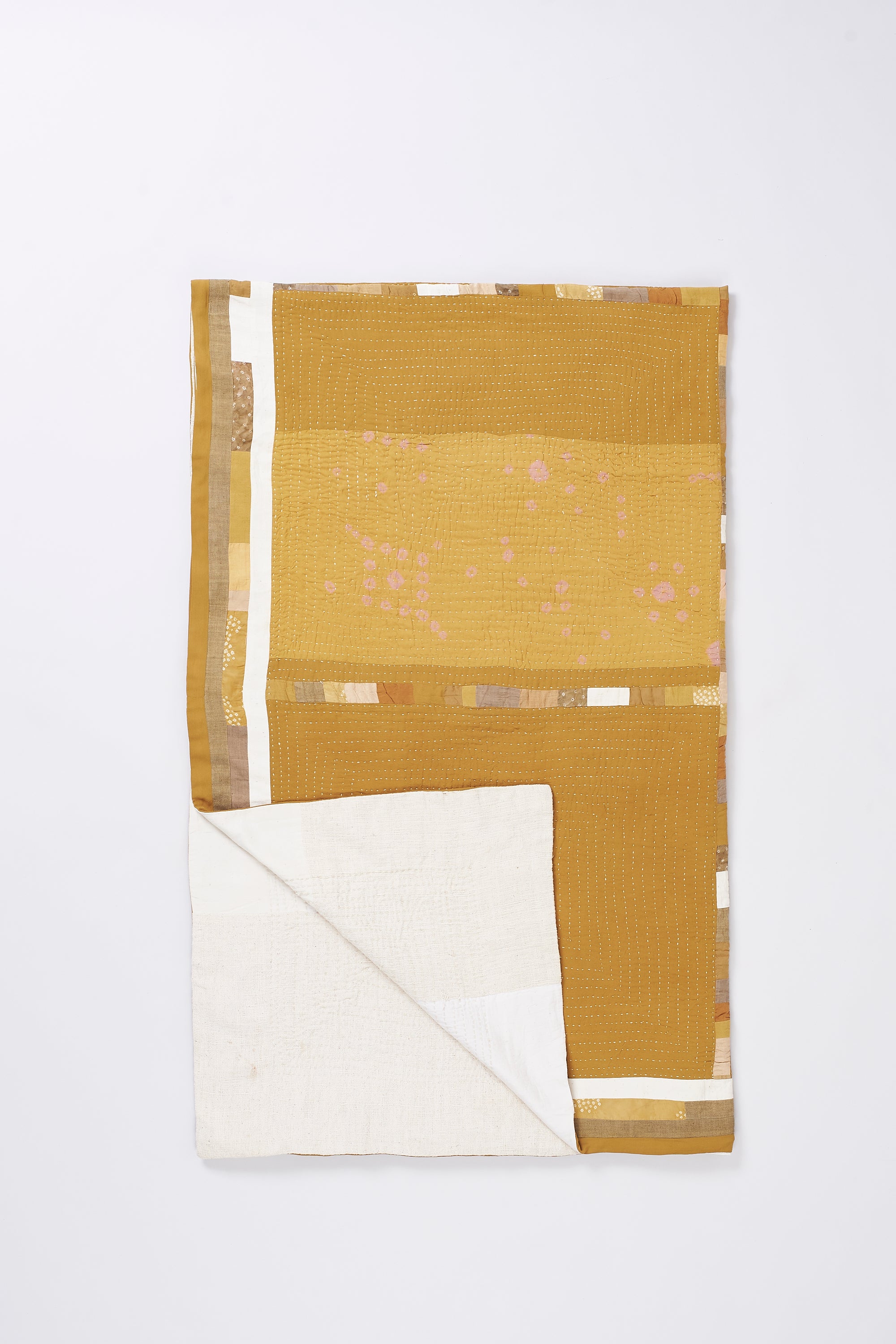 Mustard yellow quilt with white fabric with a subtle pattern on a white background