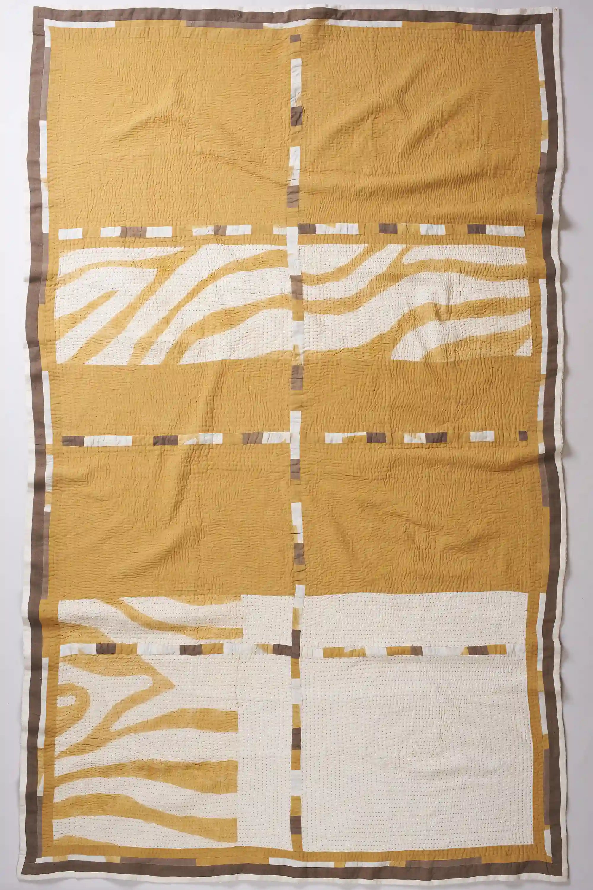 Quilt with geometric pattern in mustard yellow and white on a plain background