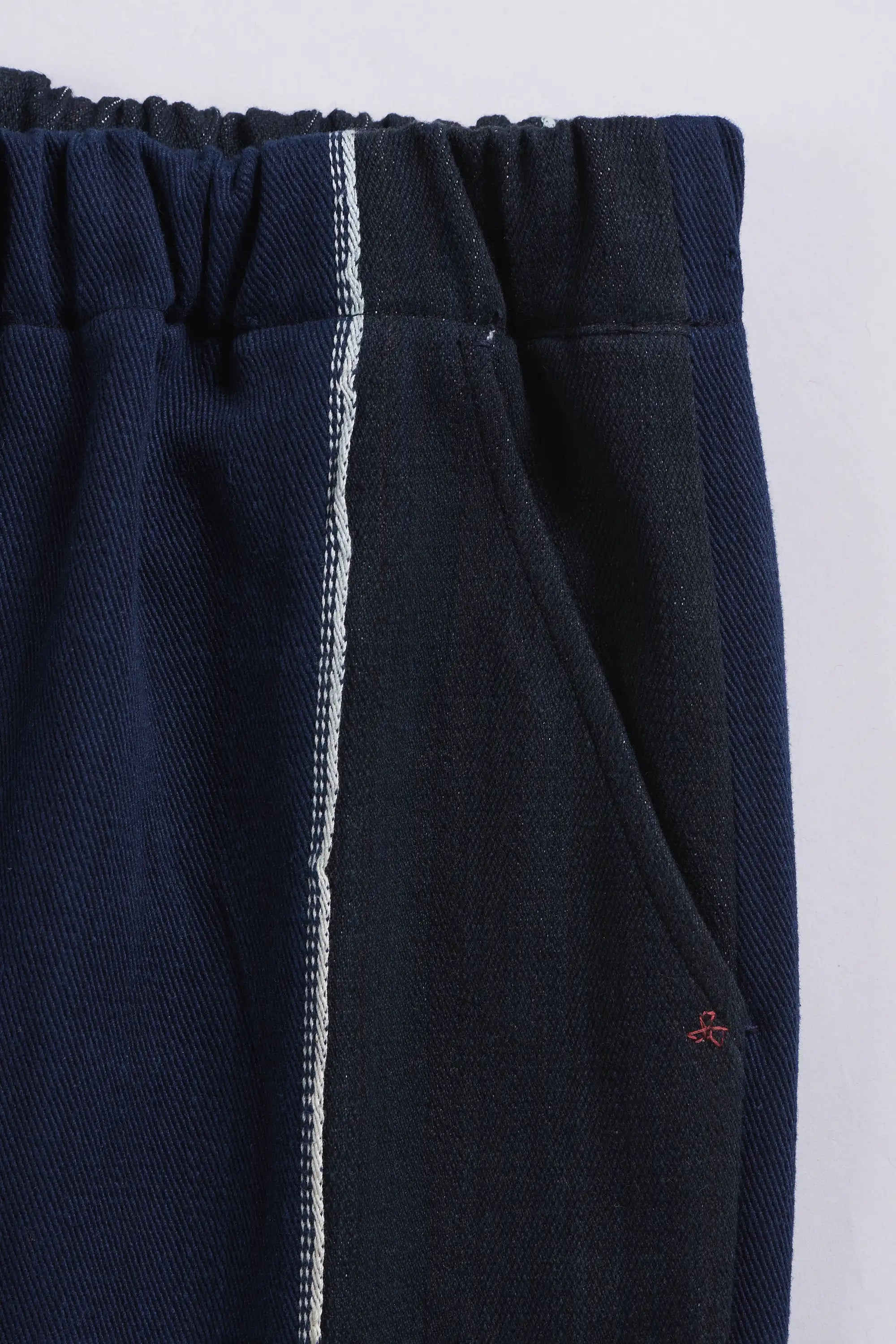 Indigo pants with a white stripe and pocket on a light grey background