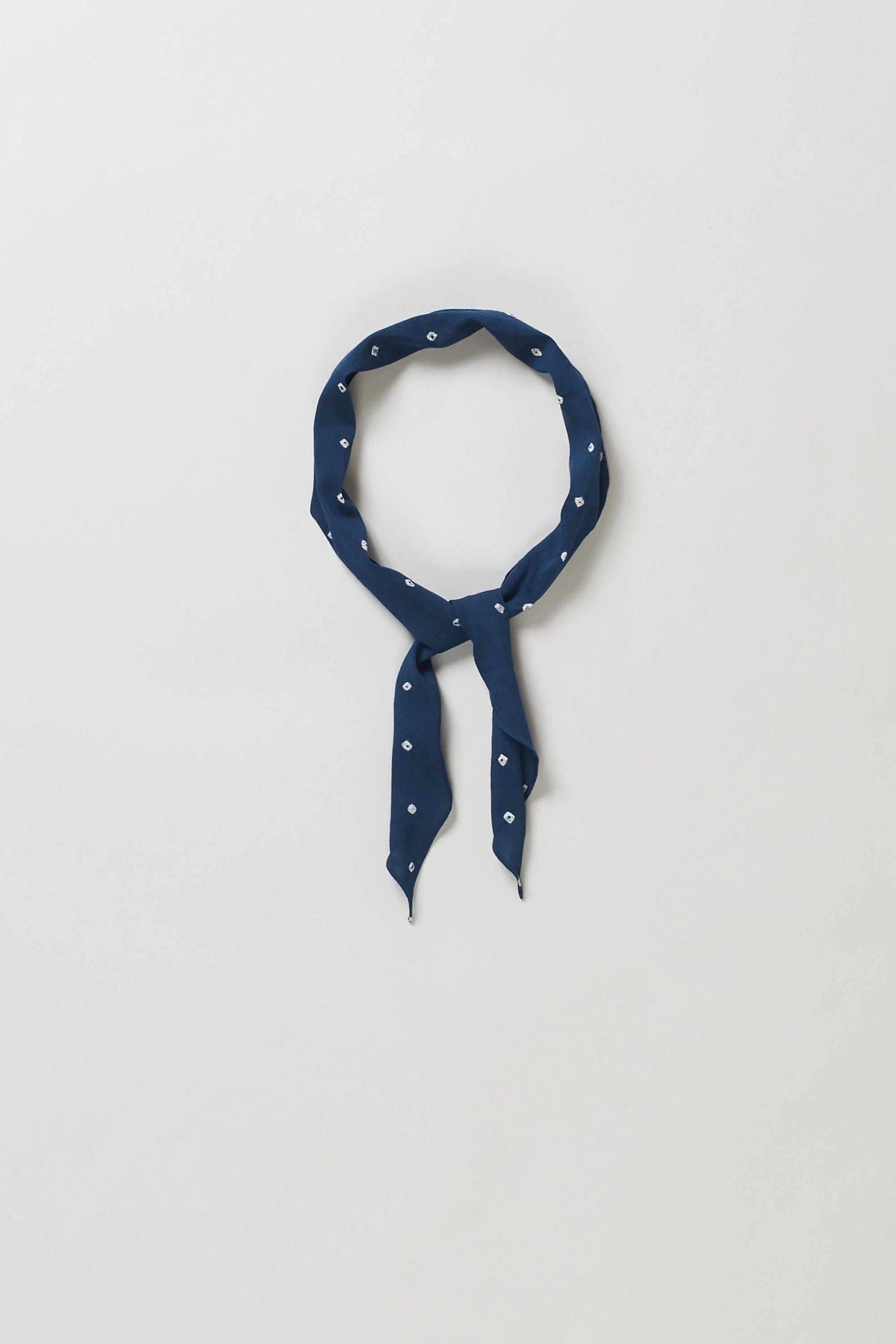 A indigo bandana with a small white polka-dot pattern, neatly folded and tied in a loop against a light grey background.