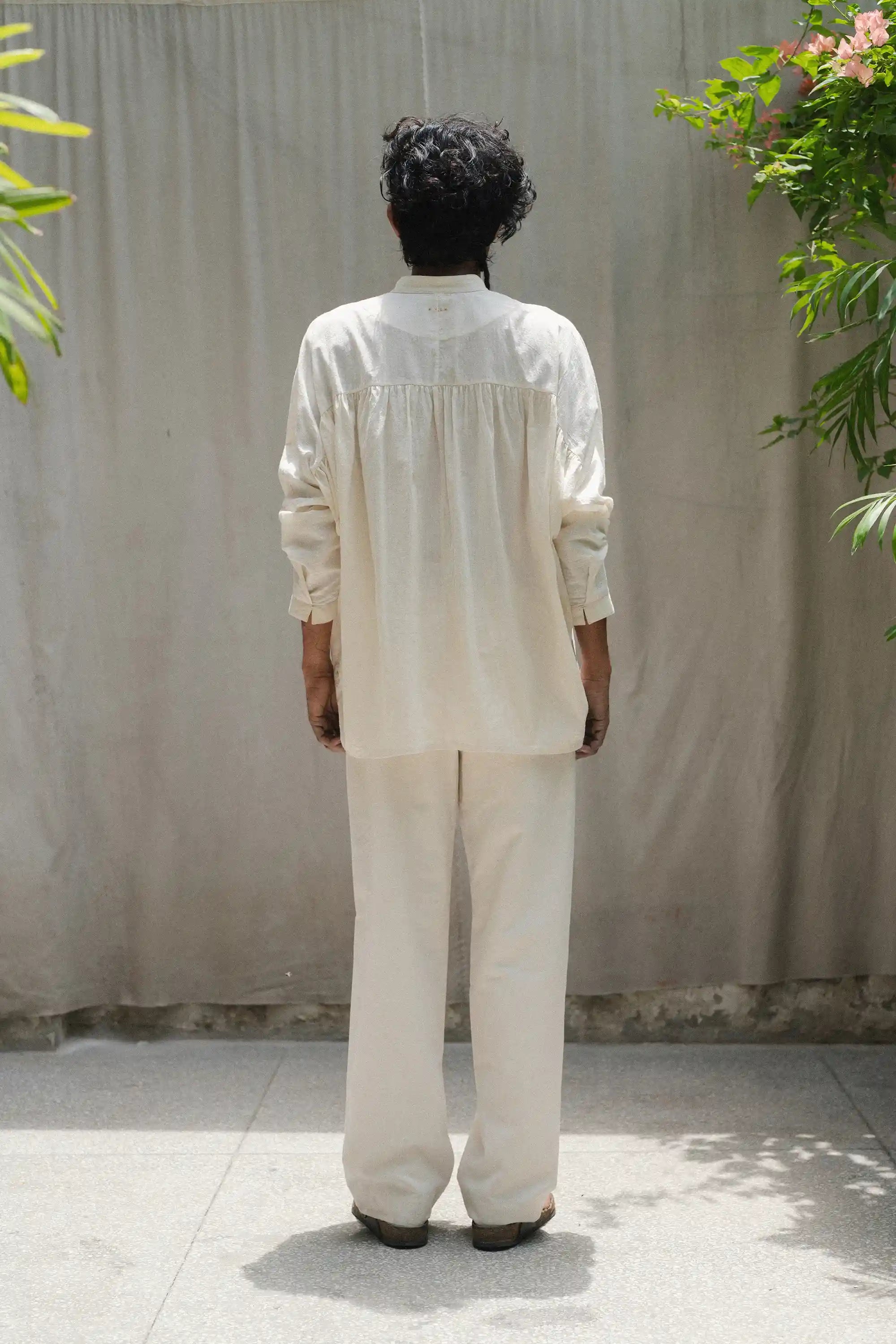 Back shot of a person wearing a ecru outfit against a plain background