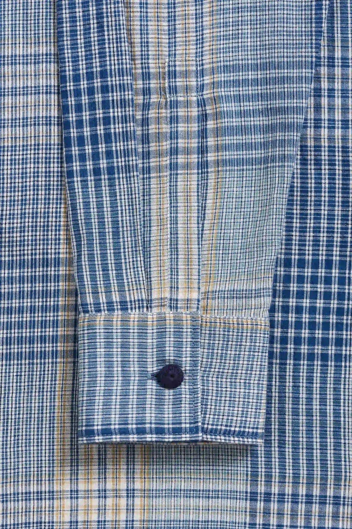 Close-up of a blue, white, and yellow plaid button-down shirt cuff with a dark navy button.