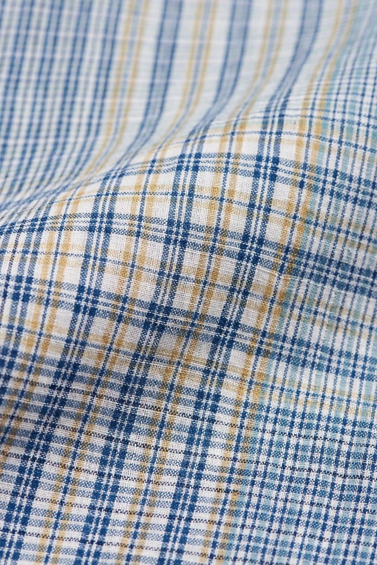 A close-up of a plaid fabric pattern with blue, white, and tan stripes, showing a soft draped texture.
