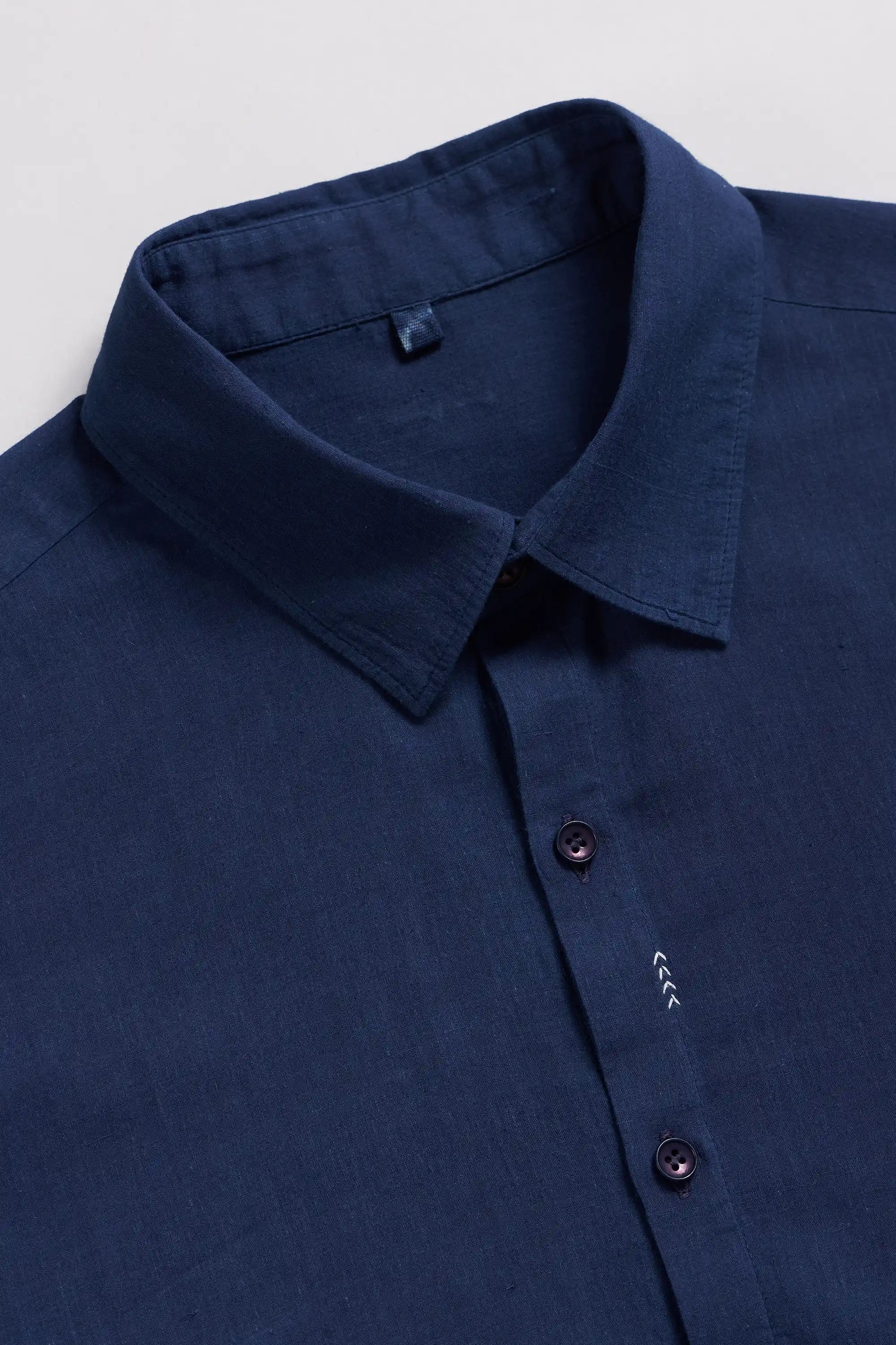 Close-up of a blue shirt with collar and buttons on a light grey background