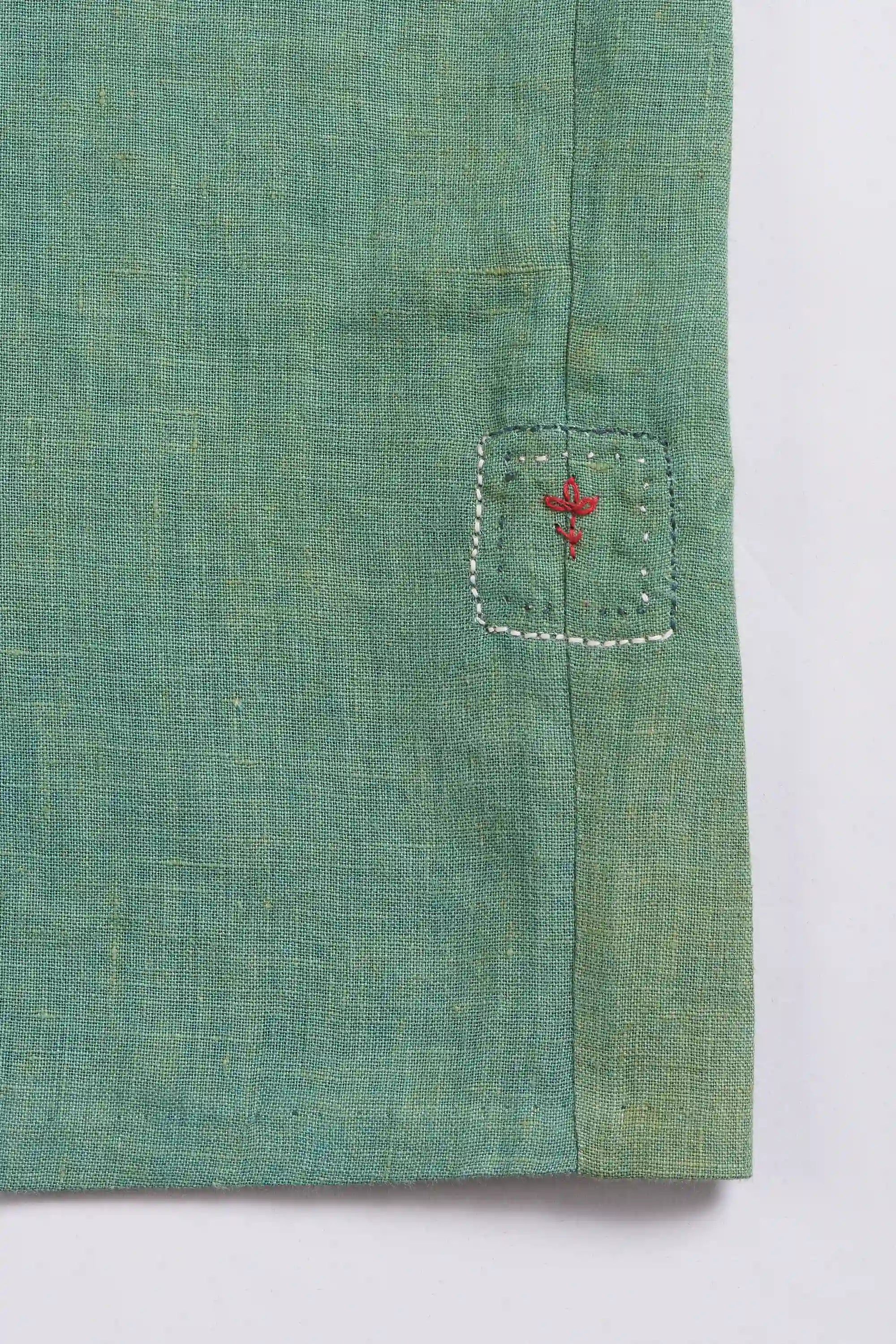 Close-up of green fabric with a small pehchan on a light grey background