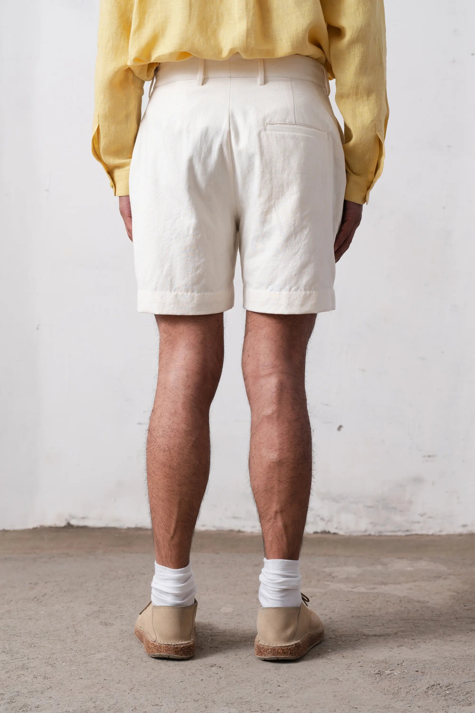 Back shot of a person wearing white shorts and a yellow shirt against a plain background