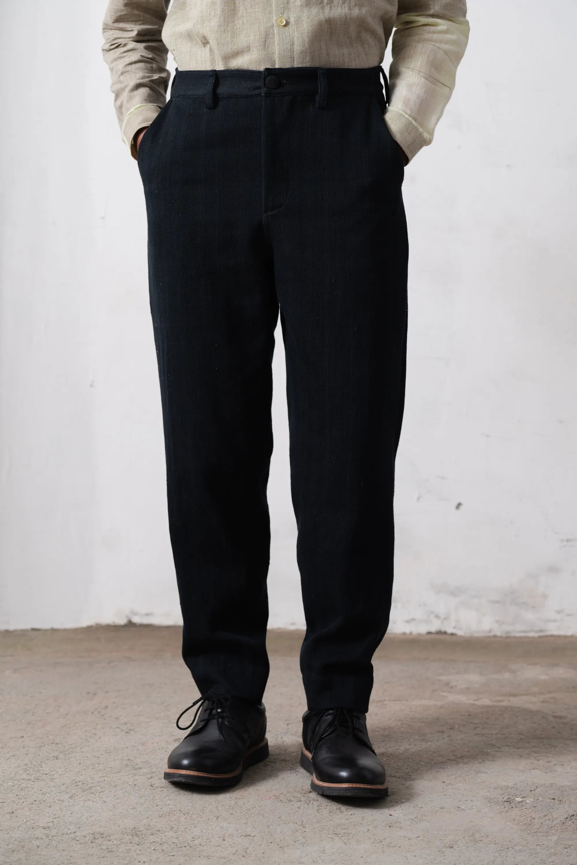 Person wearing black pants and a beige shirt against a light grey wall