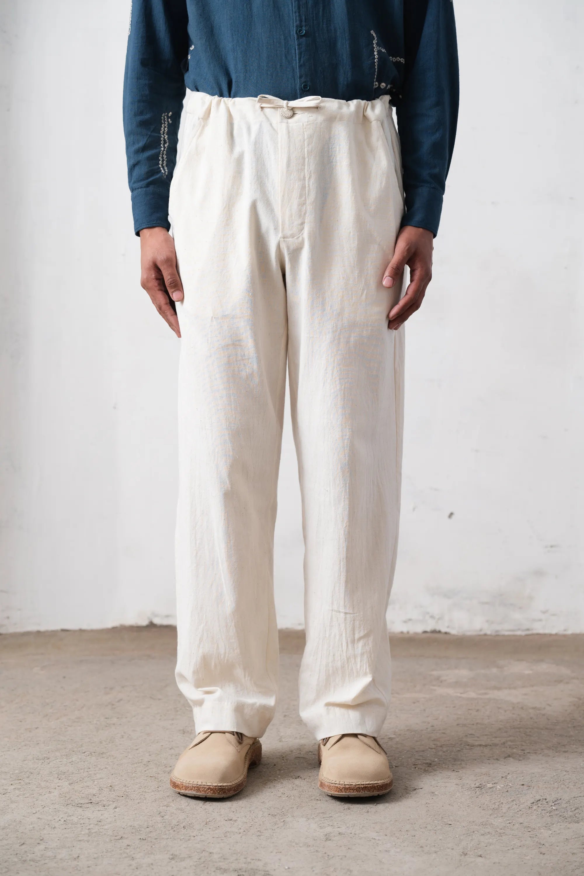 Person wearing white pants and a blue shirt against a plain background
