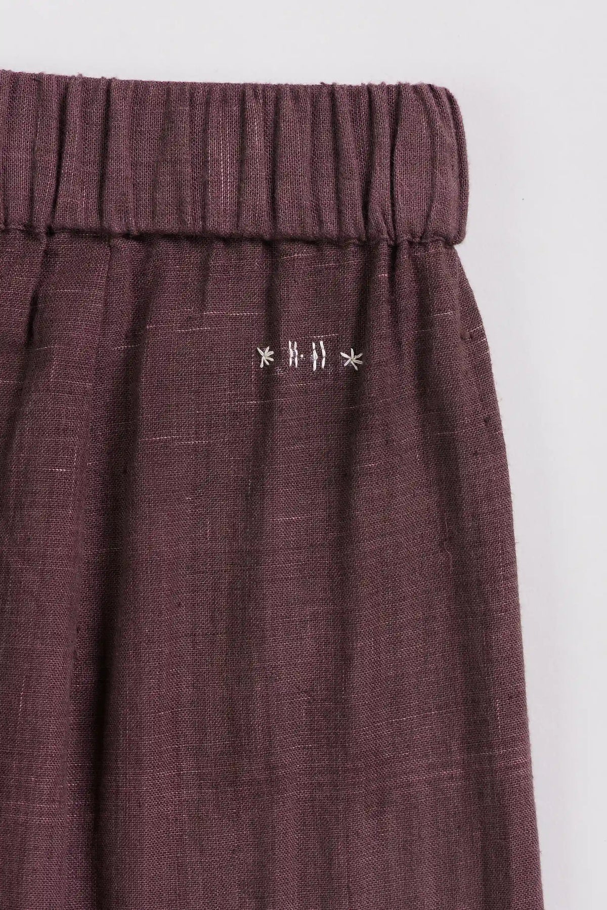 Close-up of a dark purple pleated fabric garment, showing the elastic waistband and small white embroidered star details on the front.