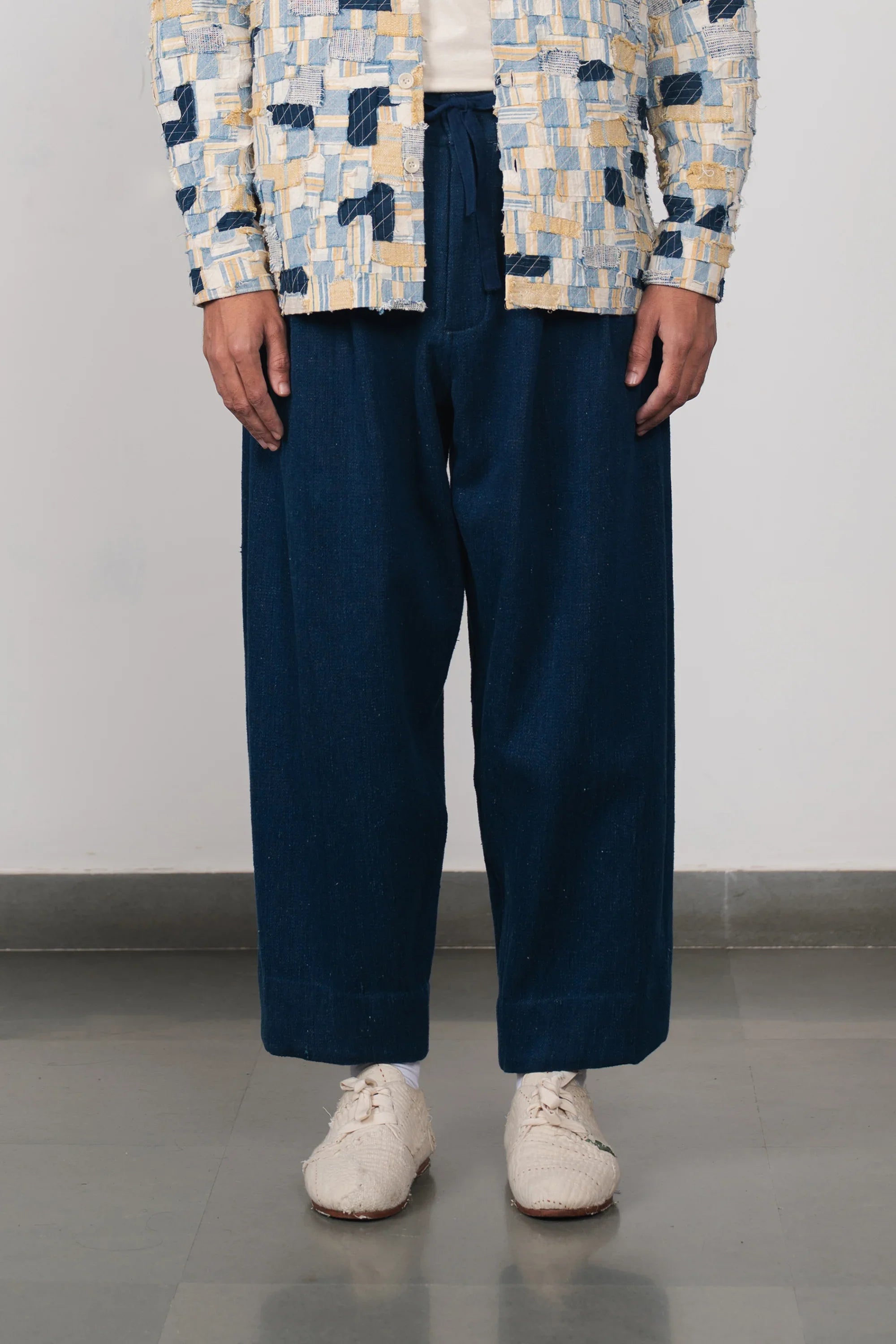 Person wearing a patterned jacket, navy pants, and white shoes on a plain background