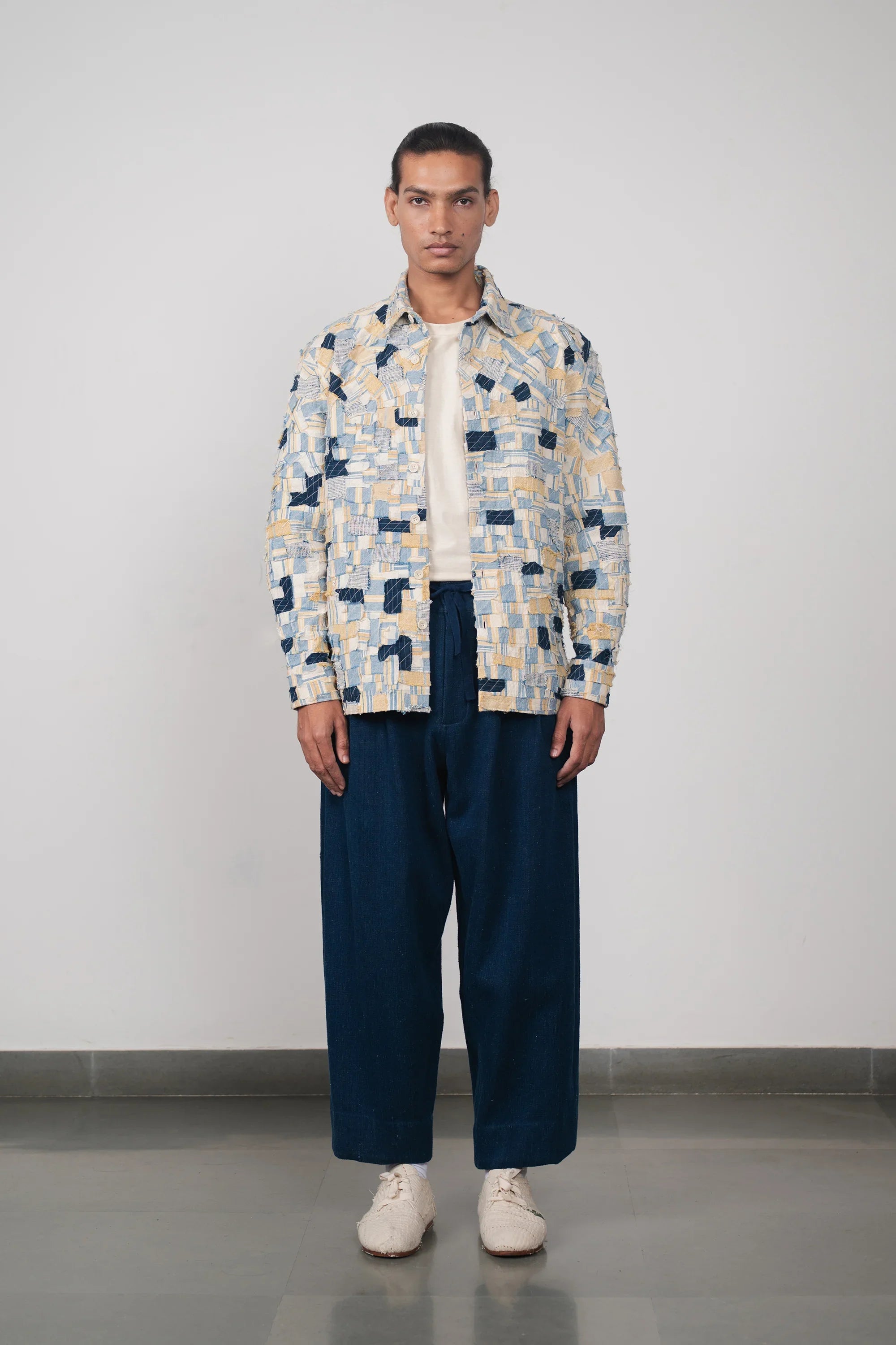 Man wearing a patterned shirt and blue pants against a plain background