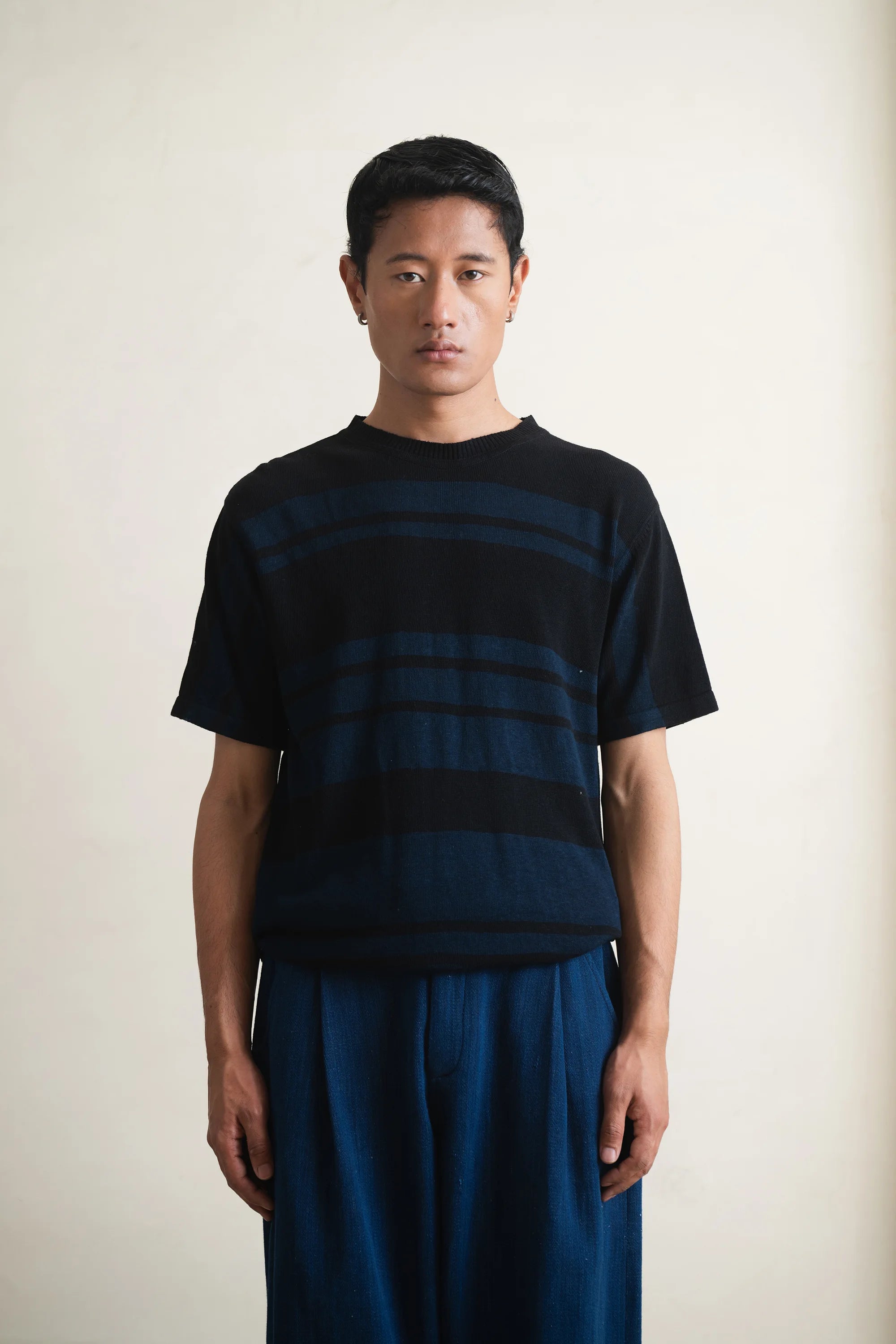 Person wearing a black and blue striped t-shirt with blue pants on a light grey background