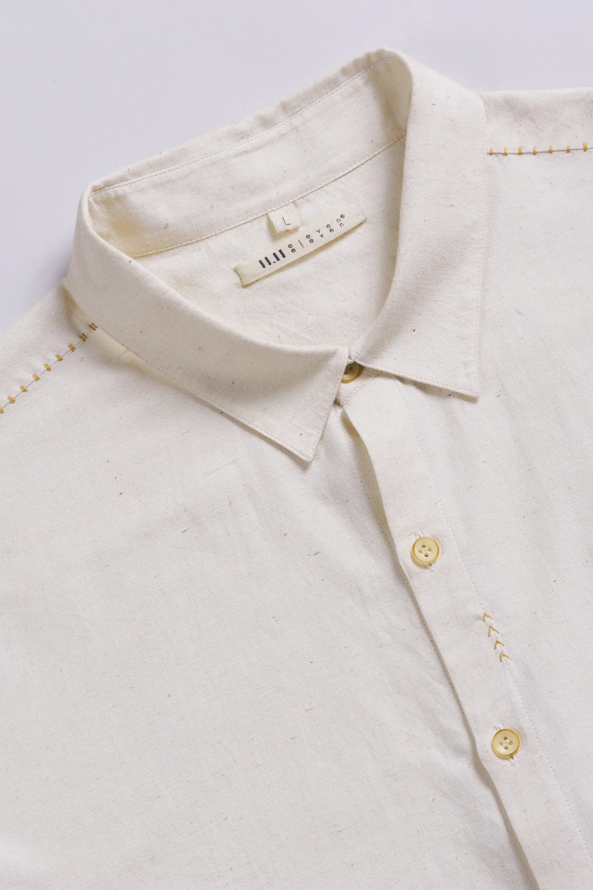Close-up of a cream-colored shirt with gold buttons and hand detailing on a light grey background