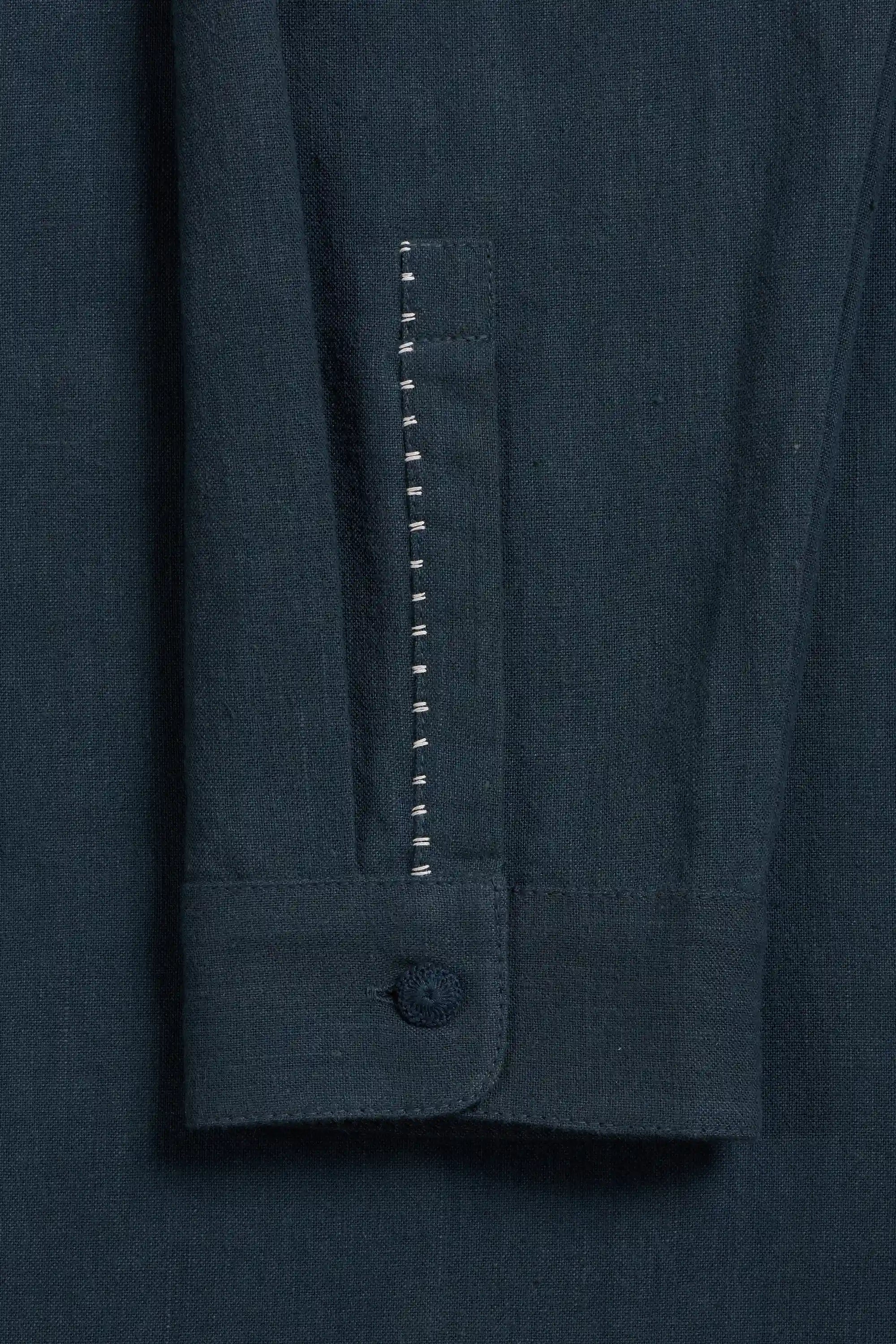 Close-up of cuff of a sleeve with a single button and a vertical decorative stitched seam.