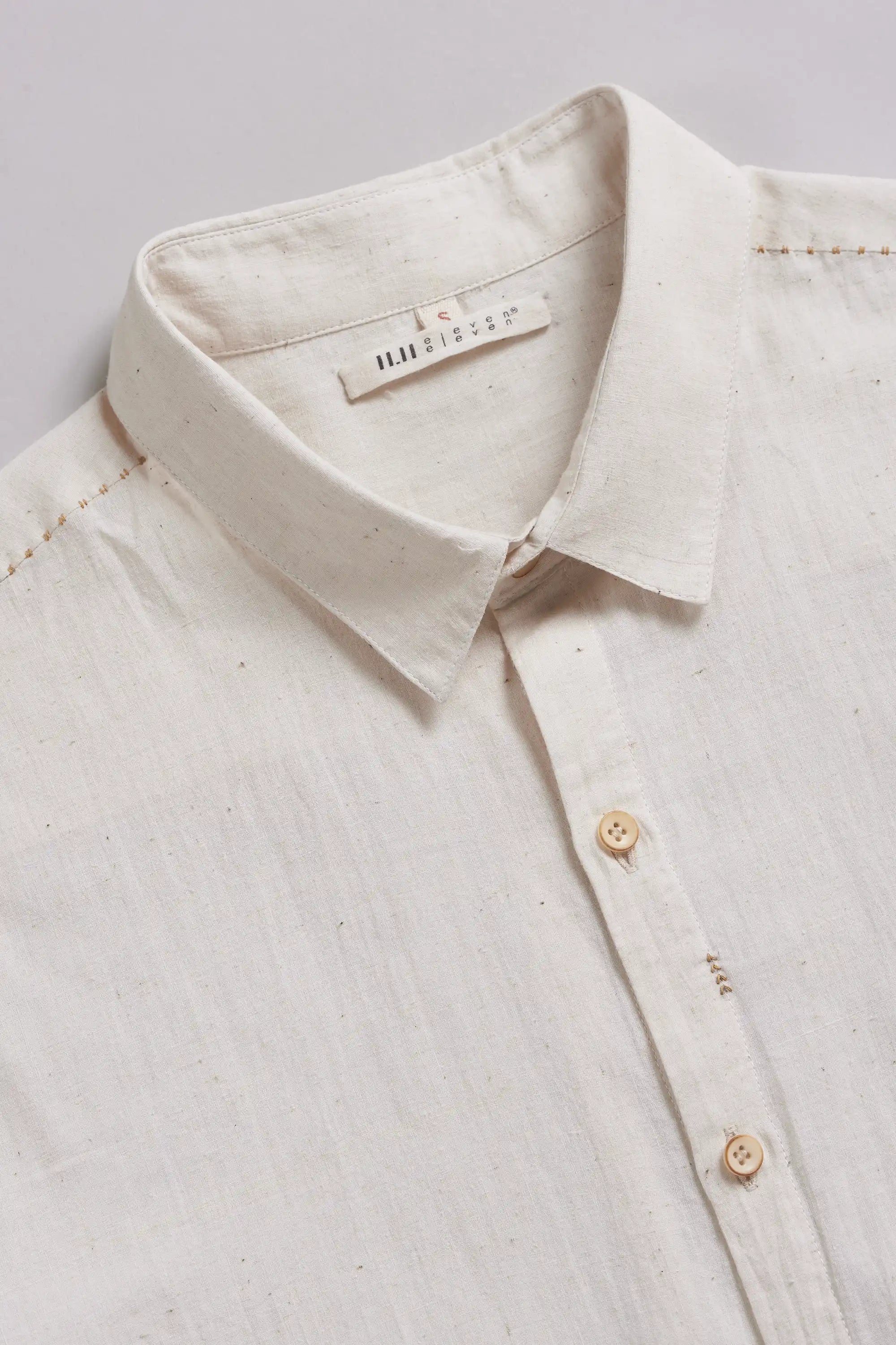 Close-up of a light-colored shirt collar with a brand label on a light grey background