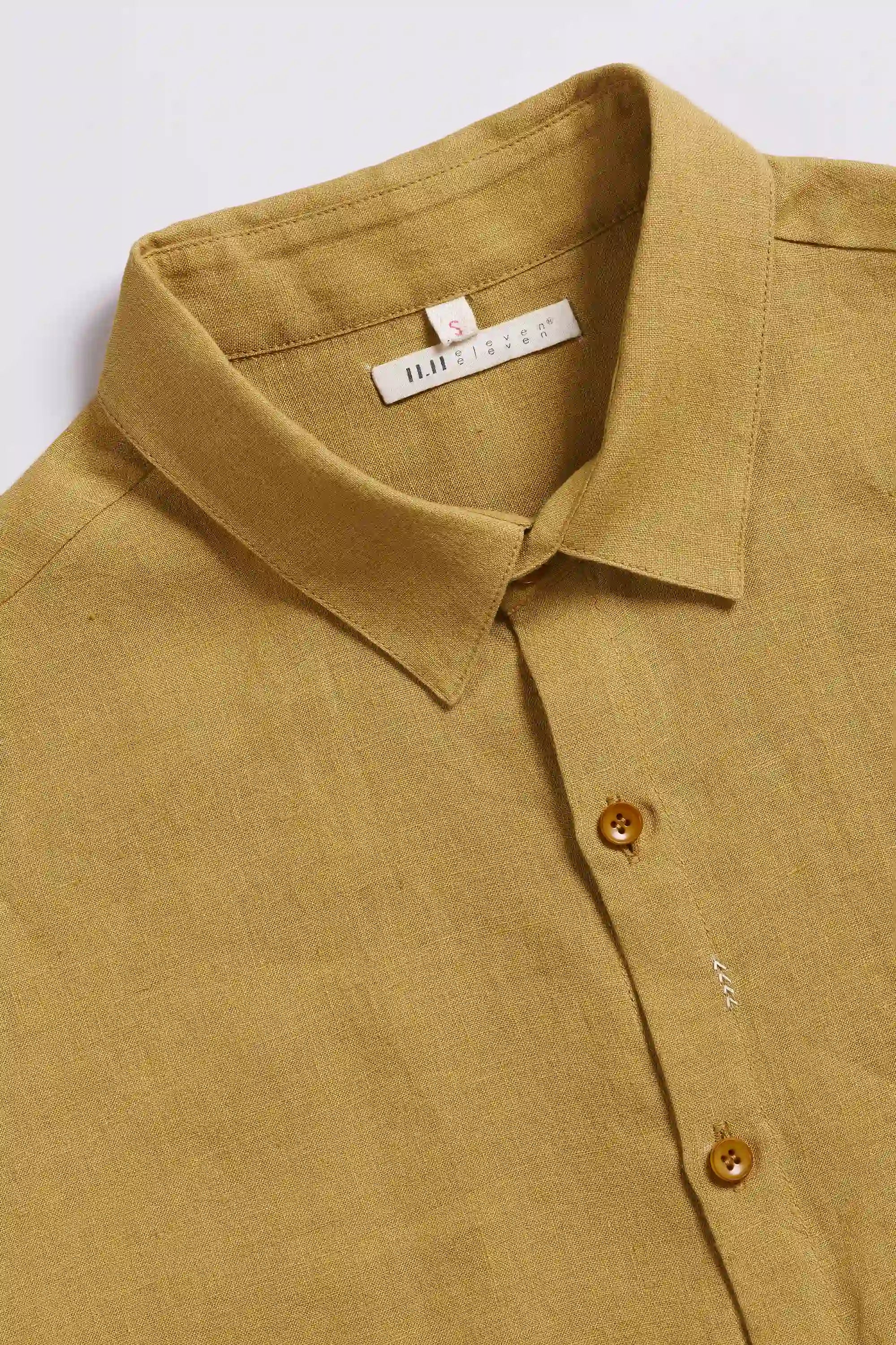 Close-up of a ochre yellow shirt with collar and buttons on a light grey background