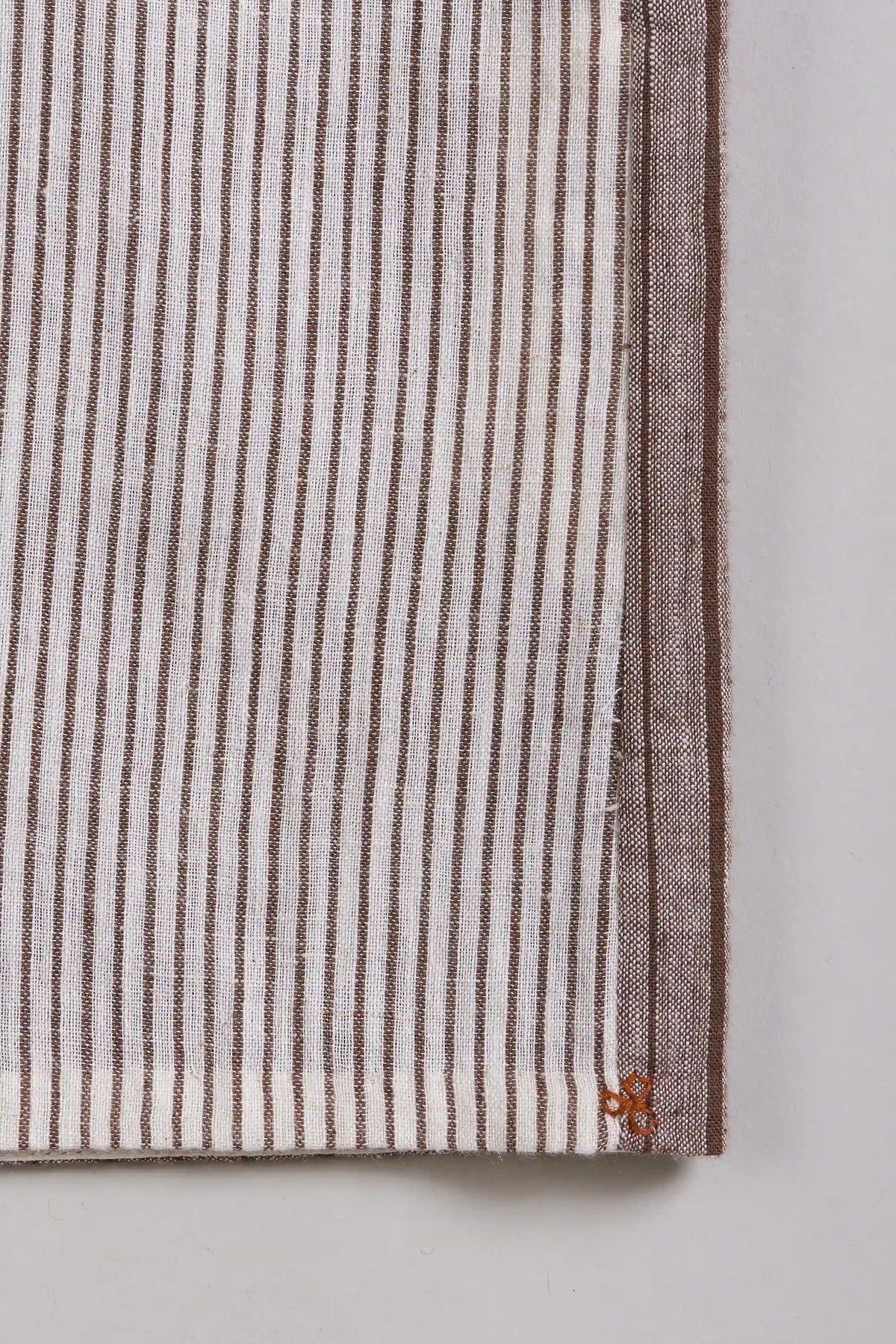 A close-up of a striped textile, featuring vertical brown and white stripes with a solid brown border on the right side.