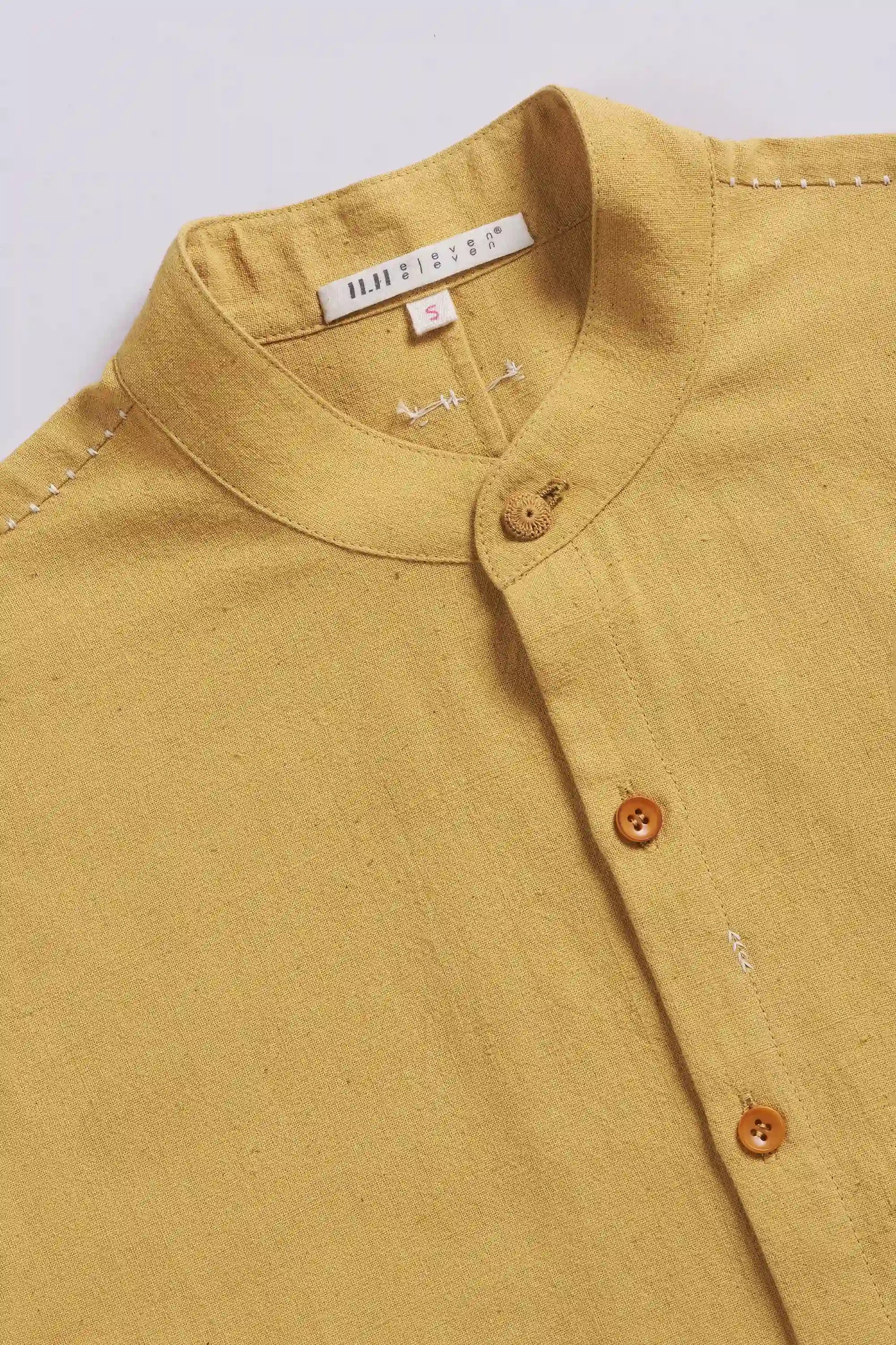 Close-up of a ochre yellow shirt with buttons on a light grey background