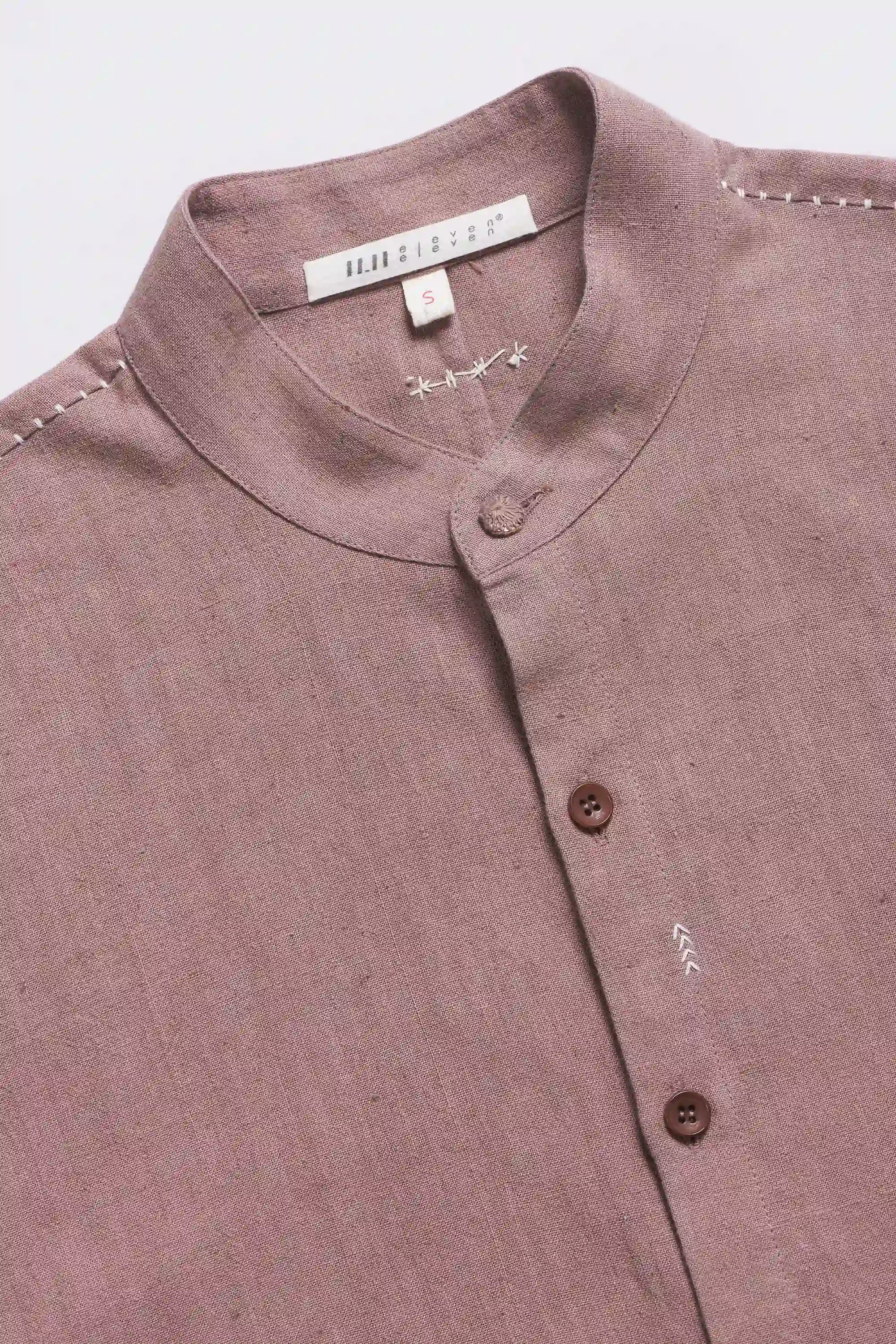 Close-up of a old rose shirt with buttons and a visible brand label on a light grey background