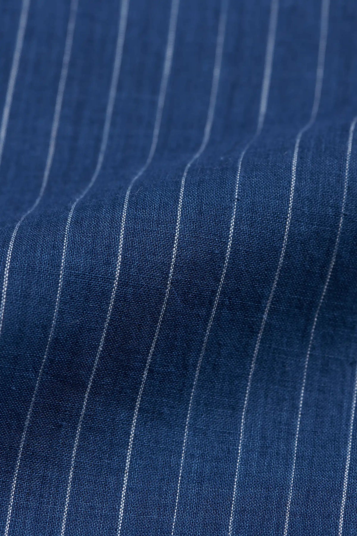 A close-up of indigo fabric with thin white vertical pinstripes.