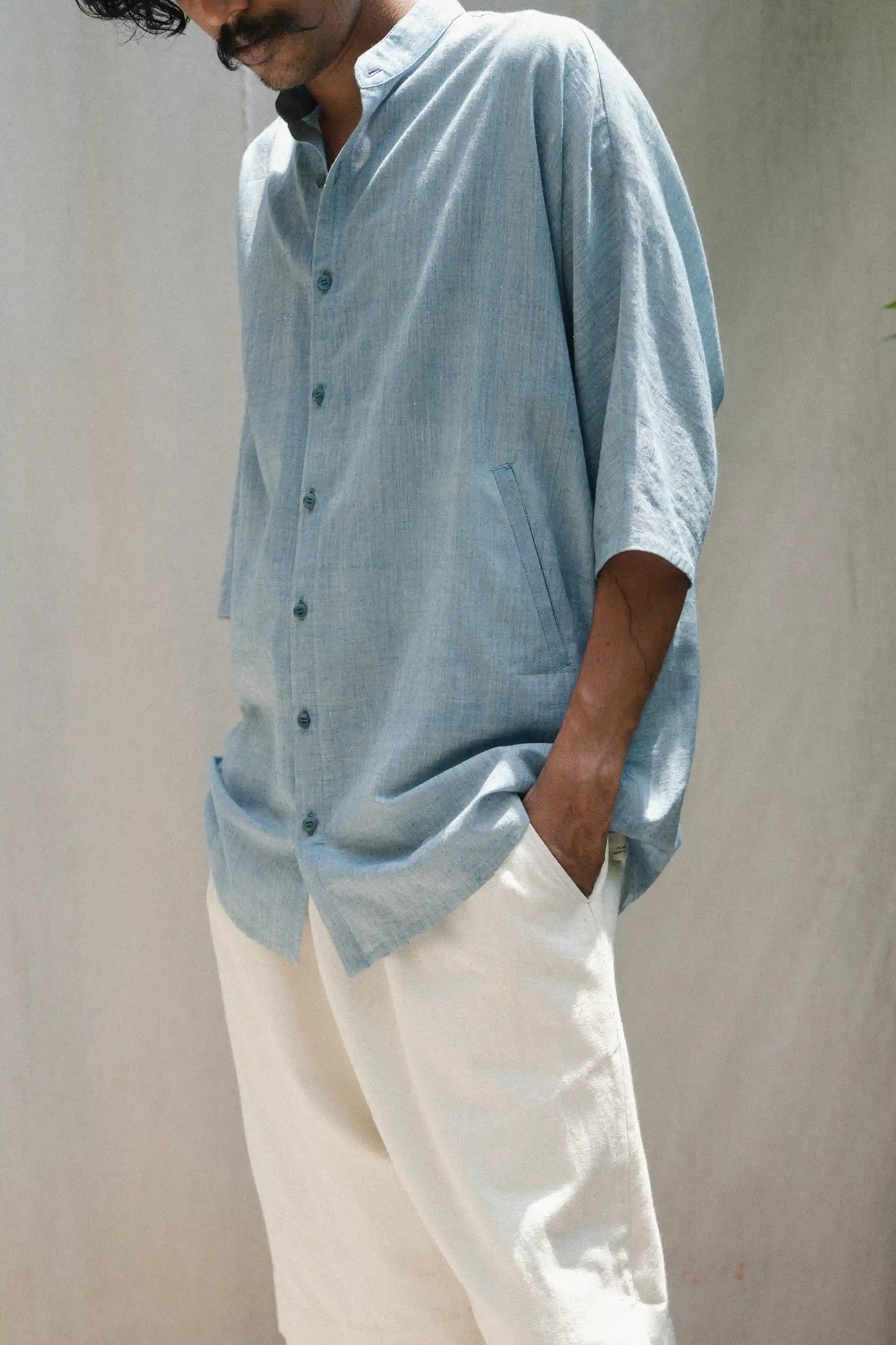 Person wearing a light blue shirt and ecru pants against a plain background