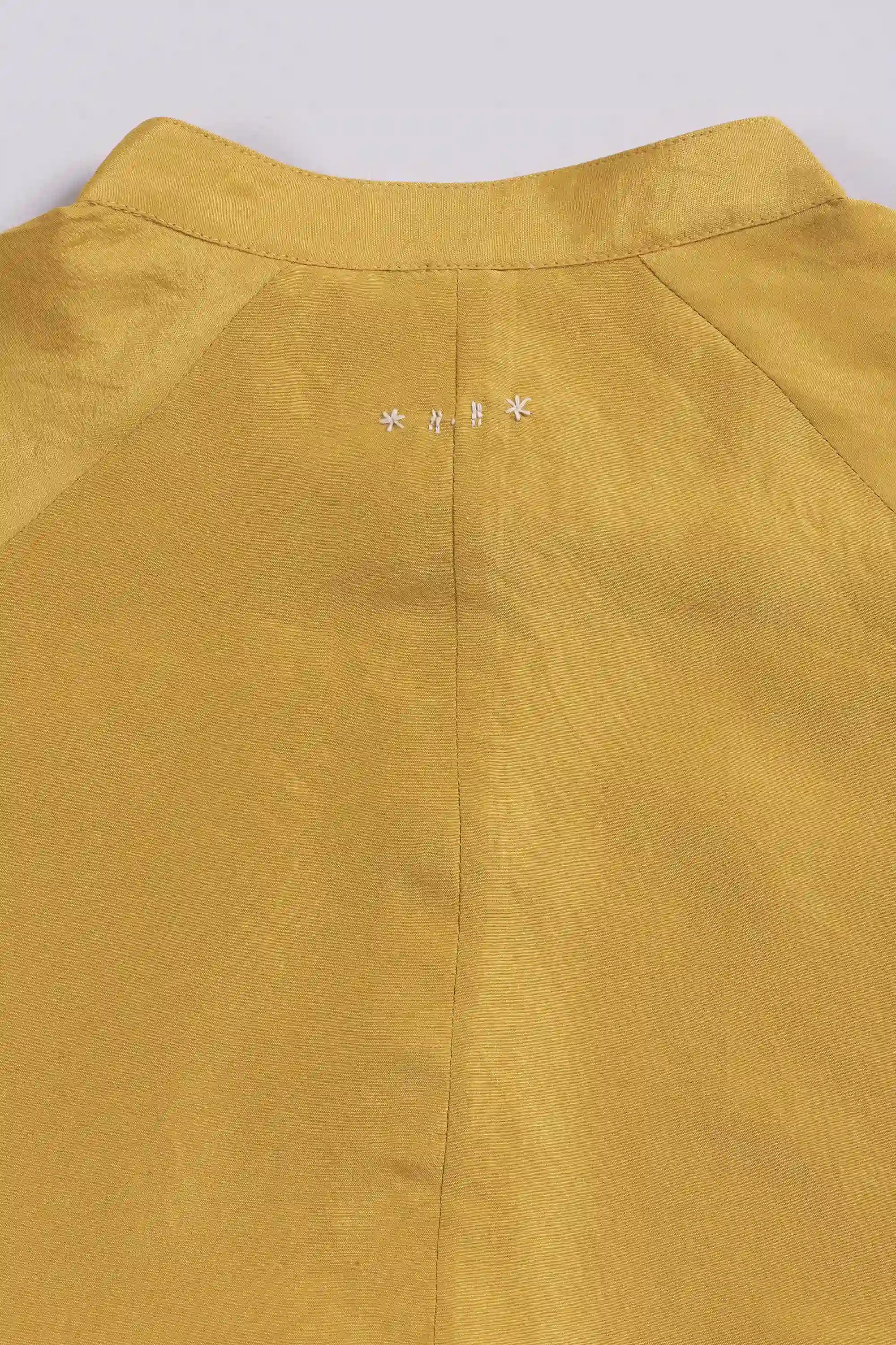 Close-up of a ochre yellow garment with a collar and hand detailing on a light grey background