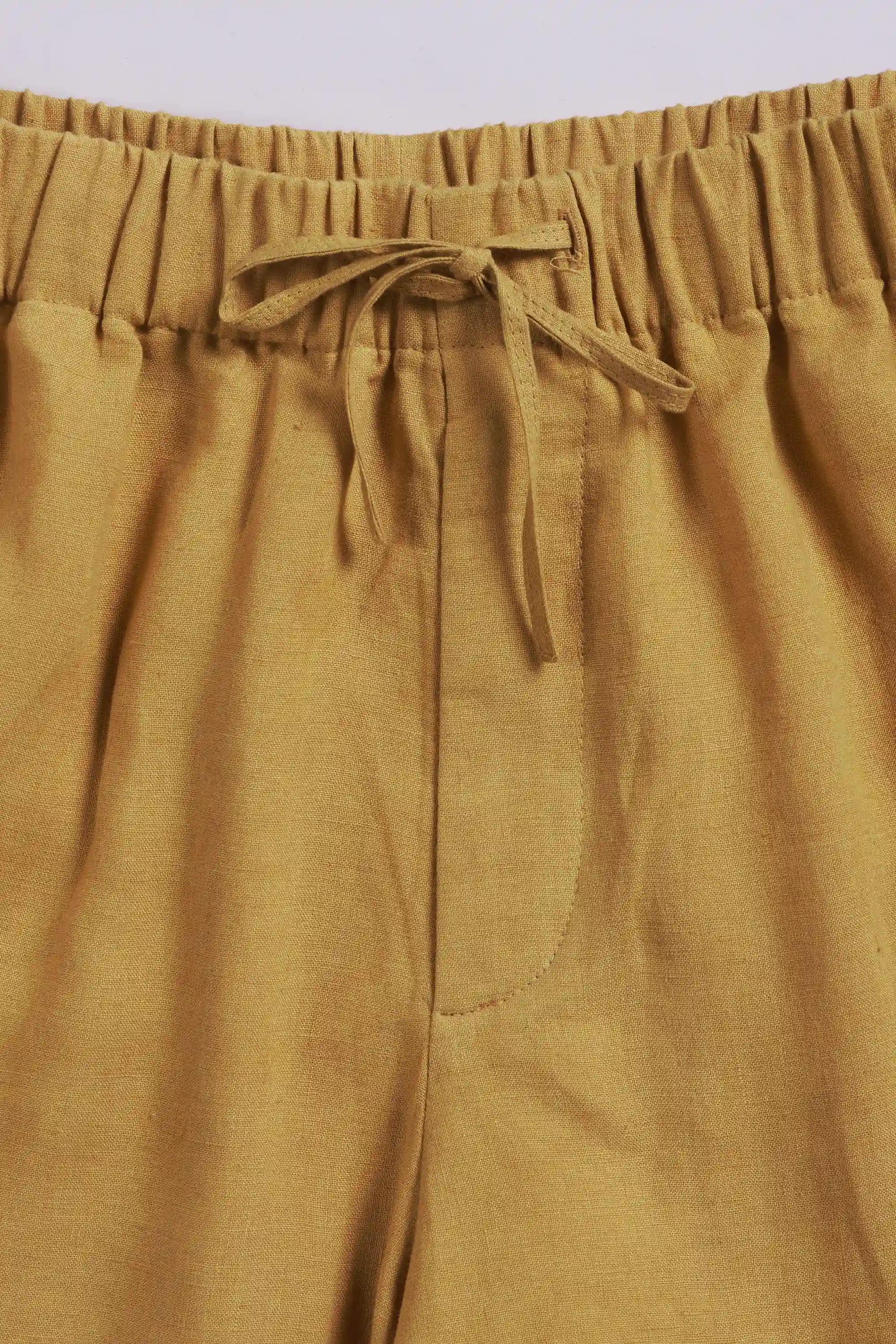 Close-up of ochre yellow pants with drawstring waistband on a light grey background