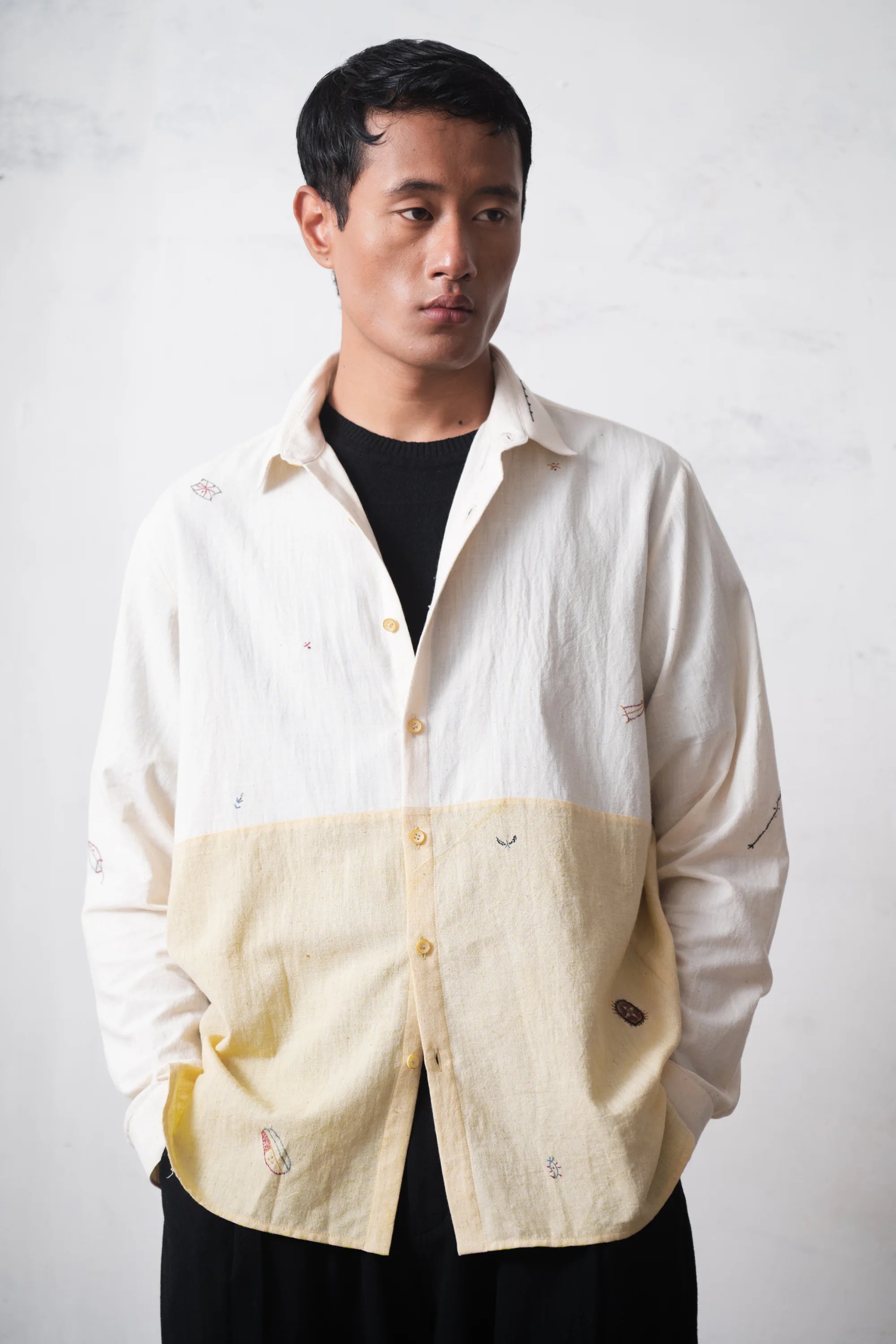 Man wearing a cream-colored shirt with a black t-shirt on a light grey background