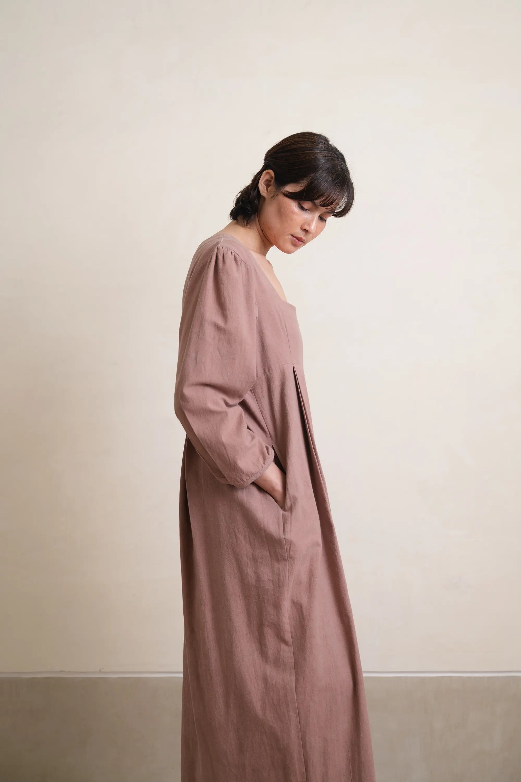 Woman wearing a long, light brown dress against a plain background