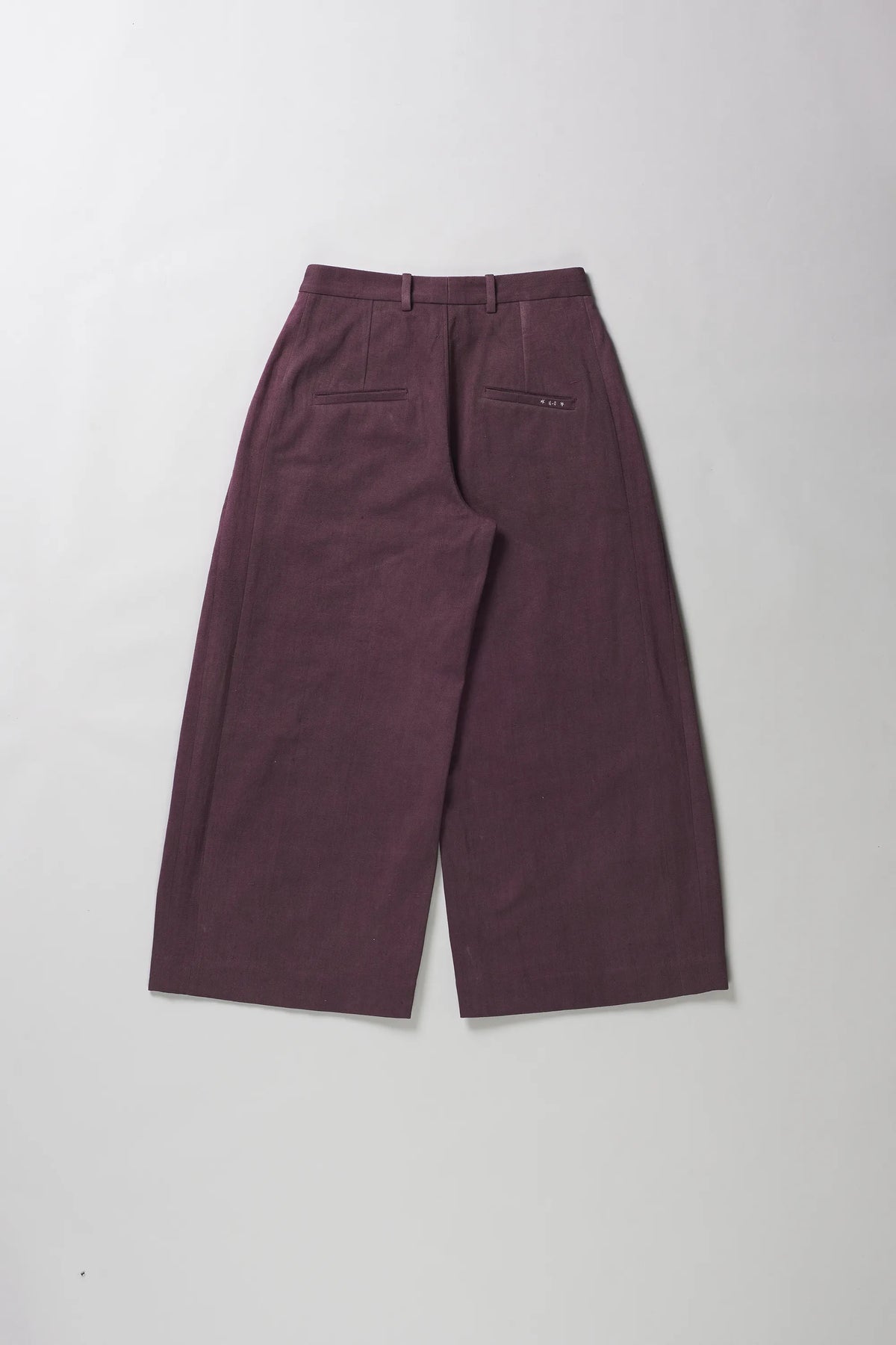 A pair of wide-leg cropped trousers in a muted plum purple color, shown from the back on a grey background.