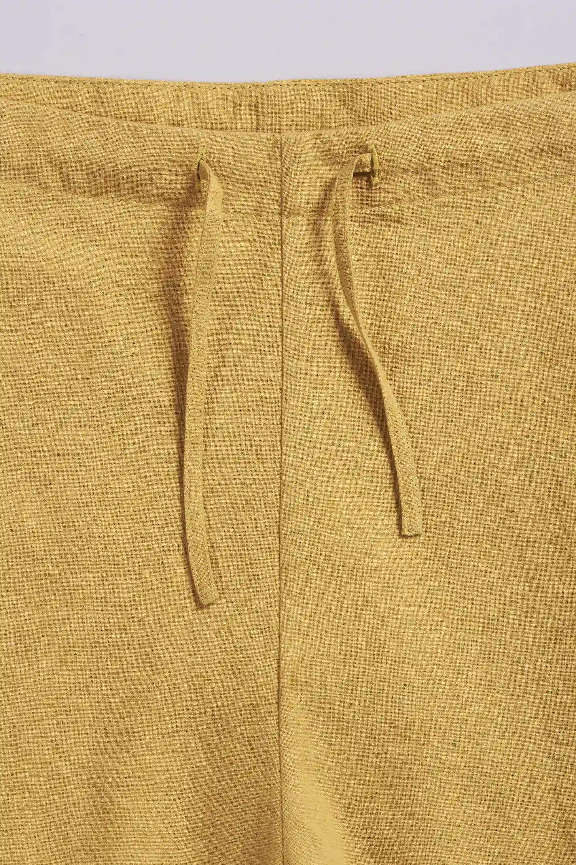 Close-up of ochre yellow pants with a drawstring on a light grey background