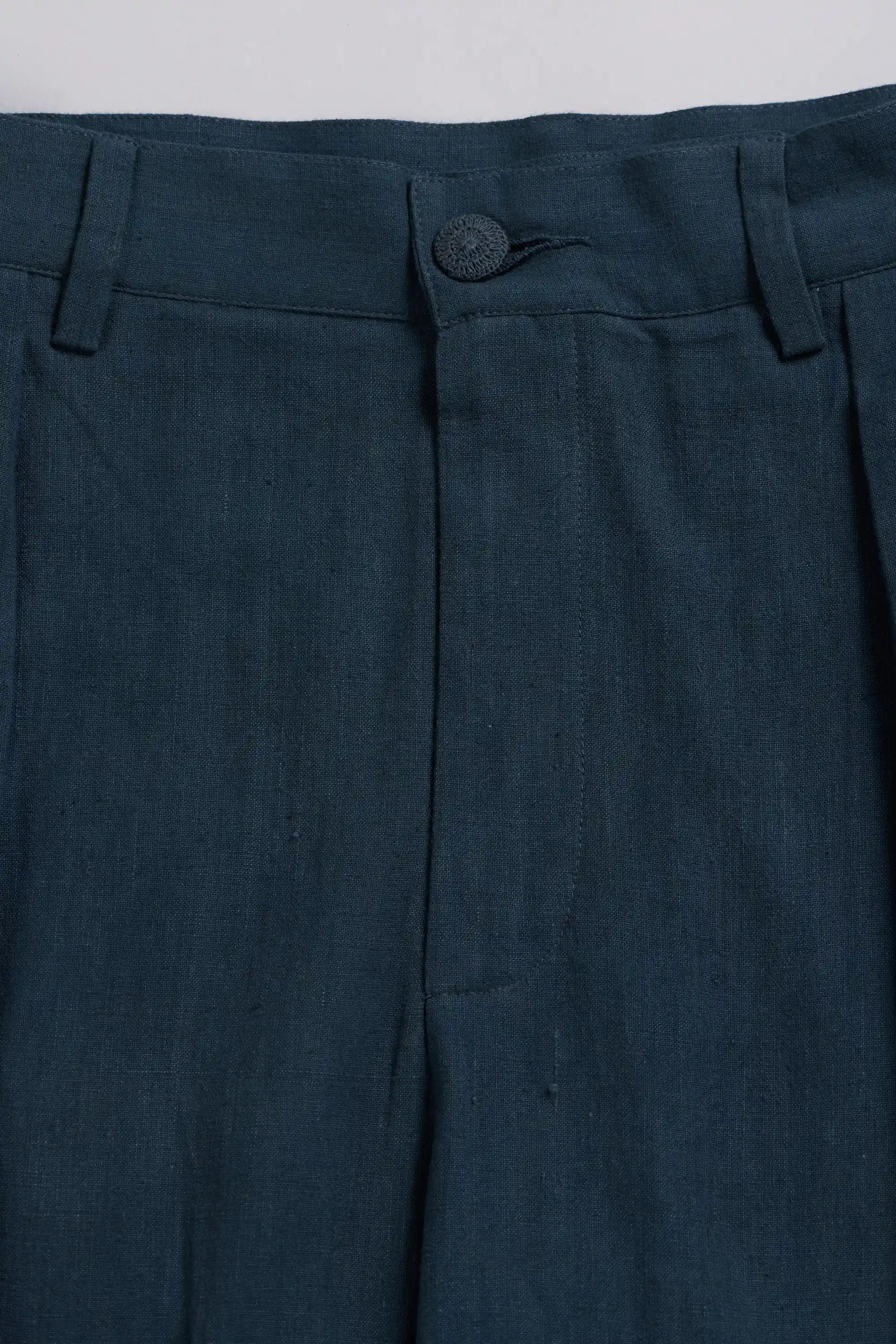 Close-up of black indigo trousers showing the waistband, button closure, belt loops, and front fly area.
