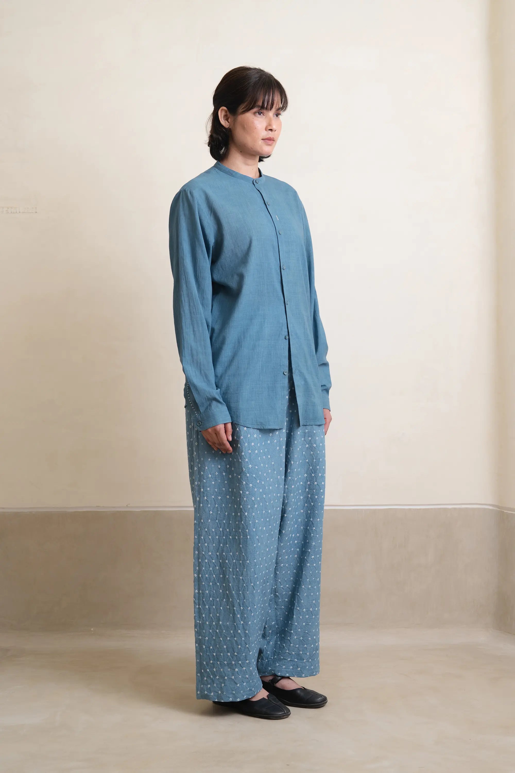 Person wearing a blue outfit with a matching top and patterned pants on a beige background