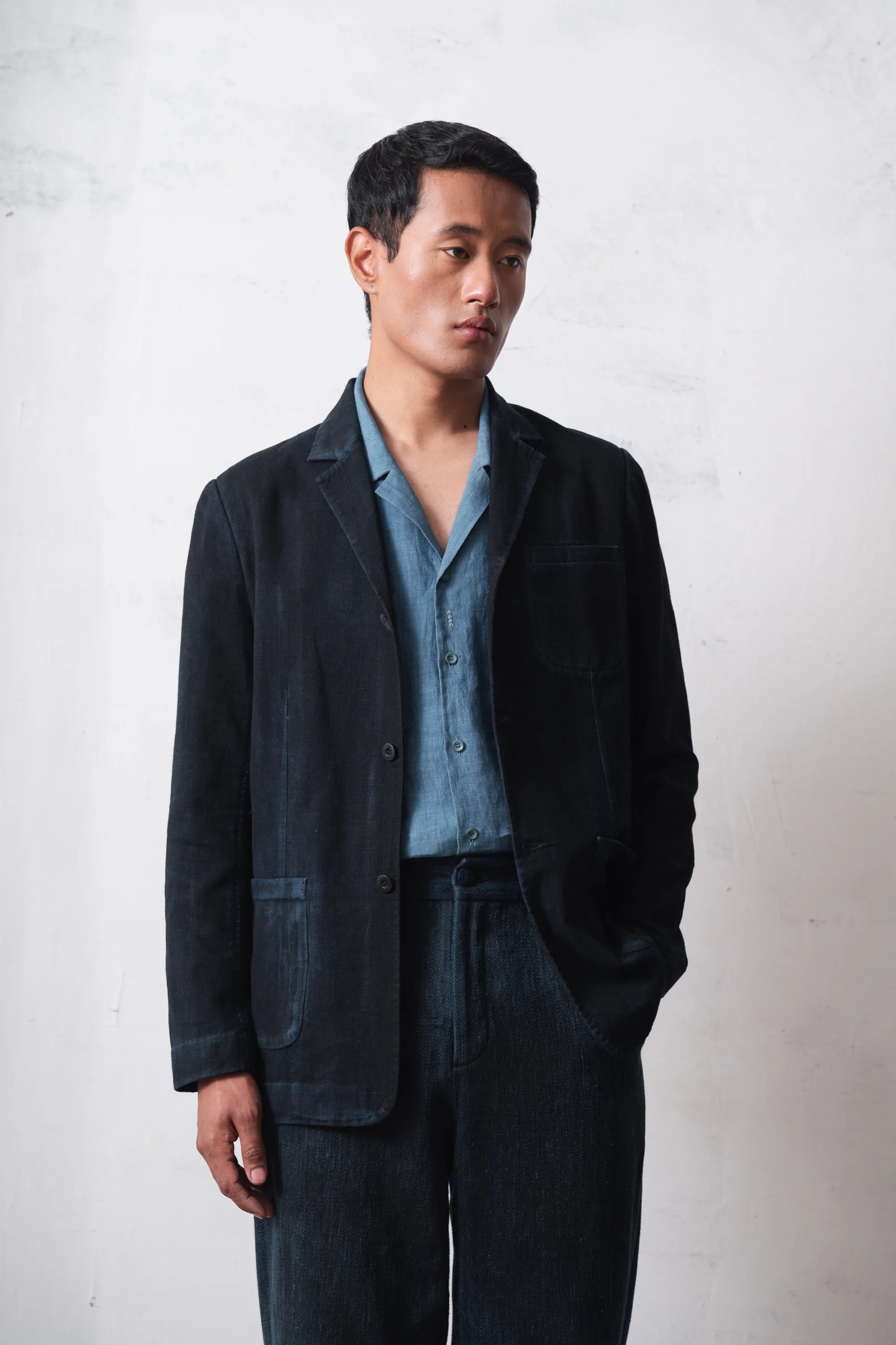 Man wearing a black jacket and light blue shirt against a light grey background
