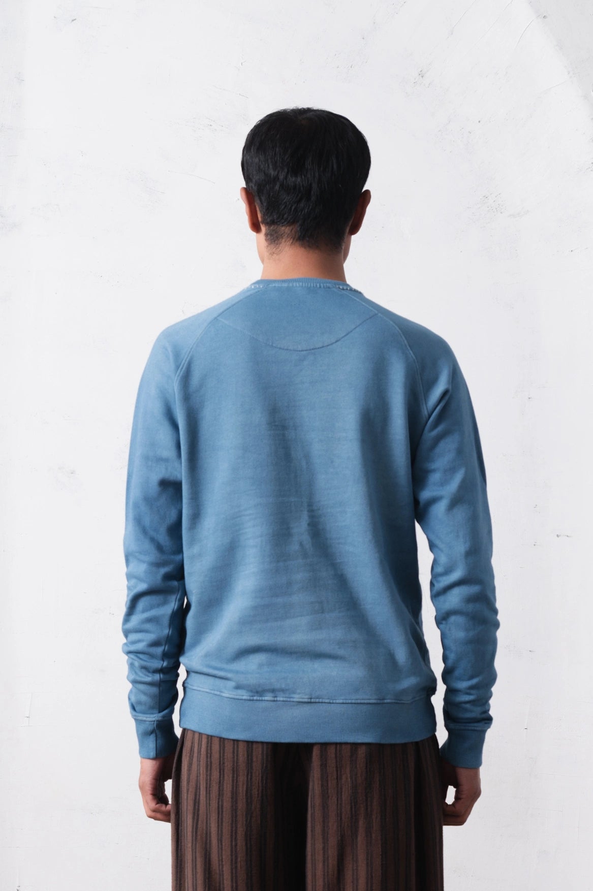Person wearing a blue sweater standing against a light grey wall