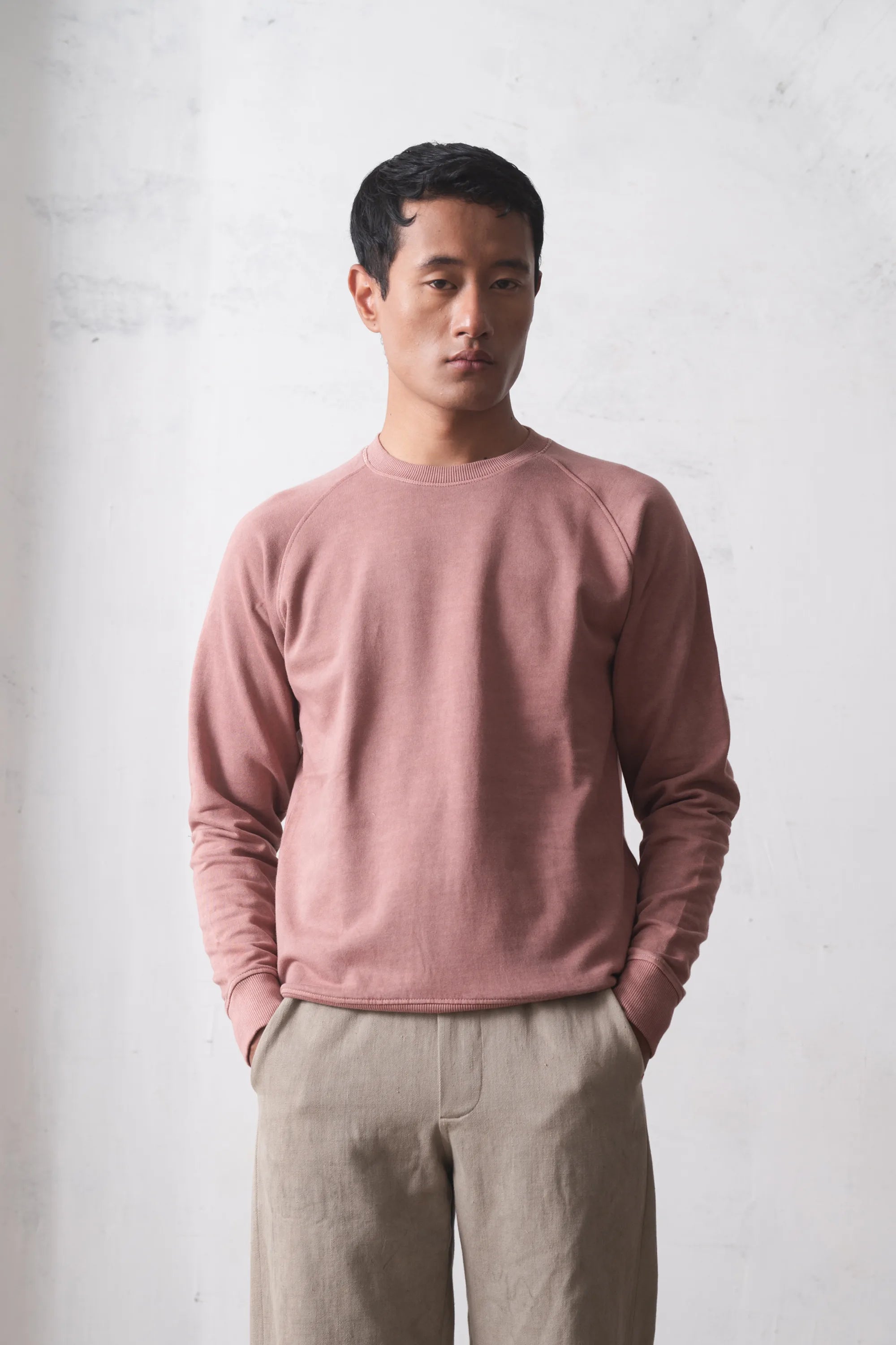 Man wearing a old rose sweater and pants against a light grey background