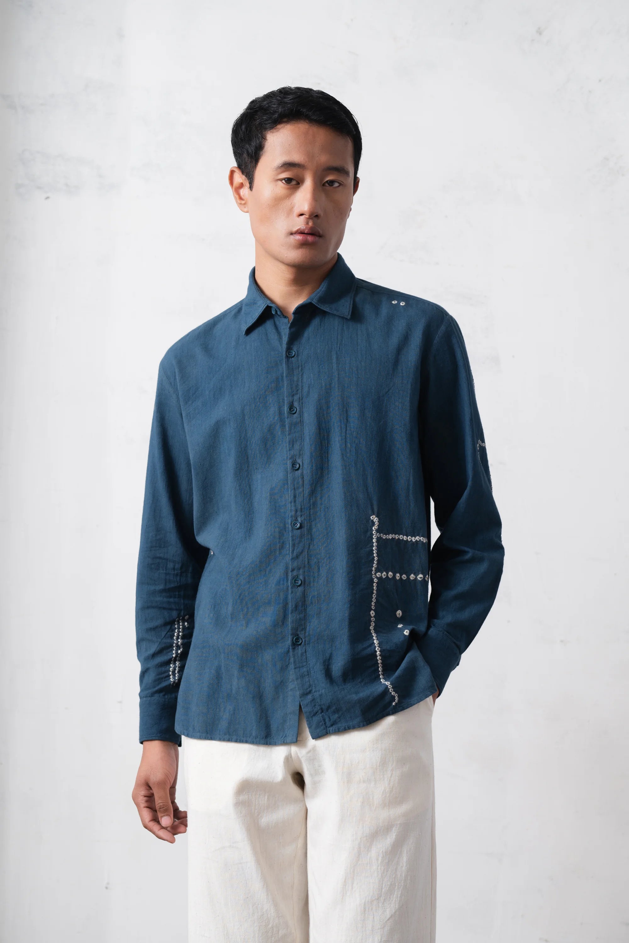 Man wearing a blue shirt with white pants against a plain background