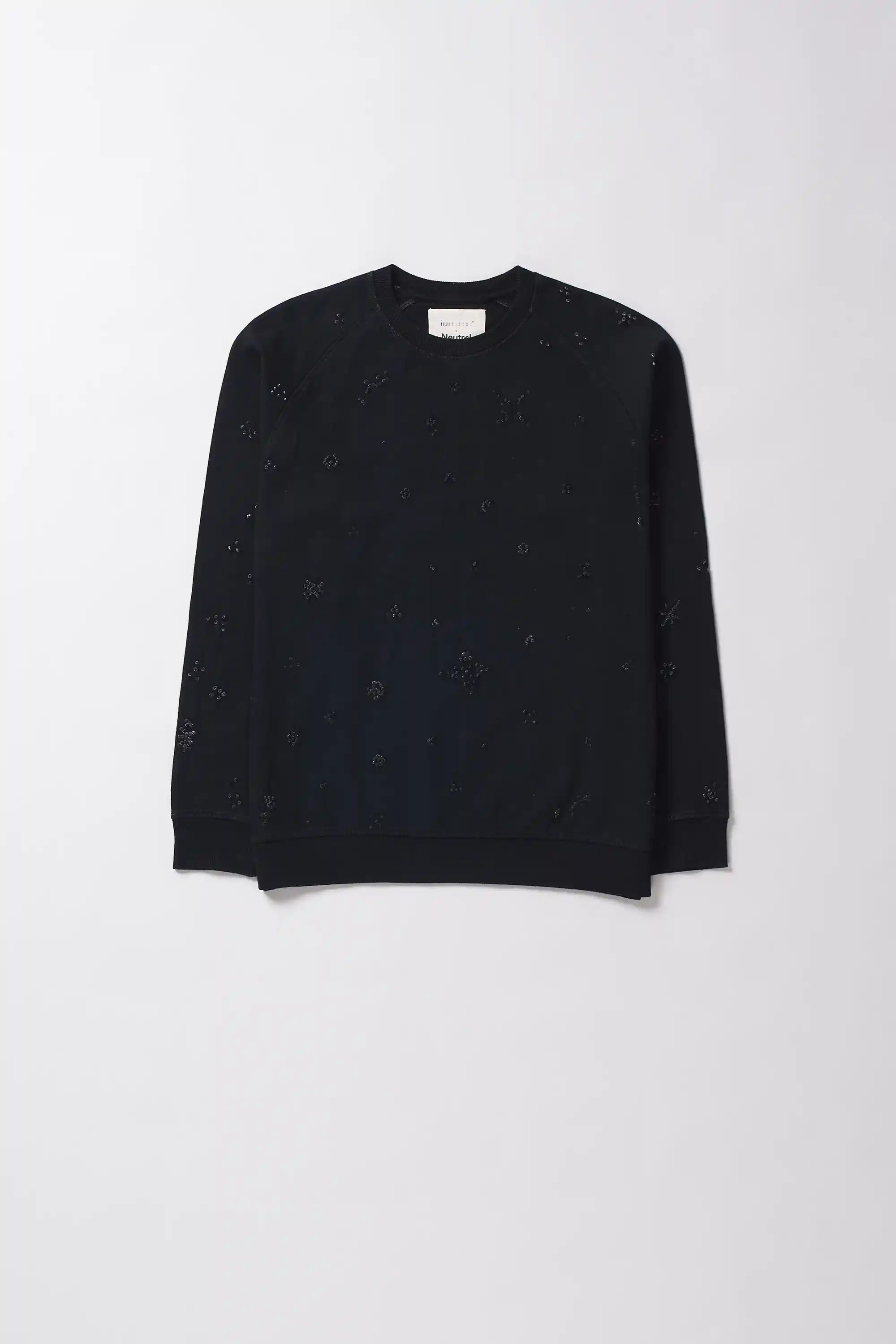 Black sweater with gold embellishments worn by a person against a neutral background