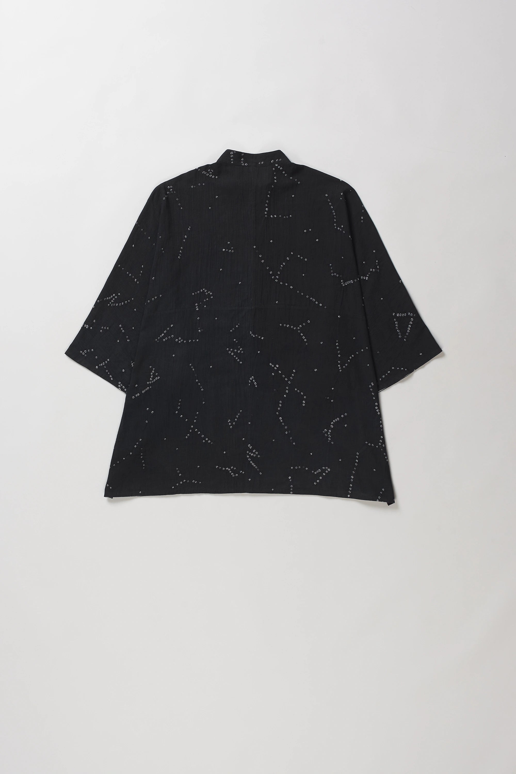 Back shot of black short-sleeve button-up shirt with an all-over white line-art constellation pattern bandhani, laid flat against a light grey background.