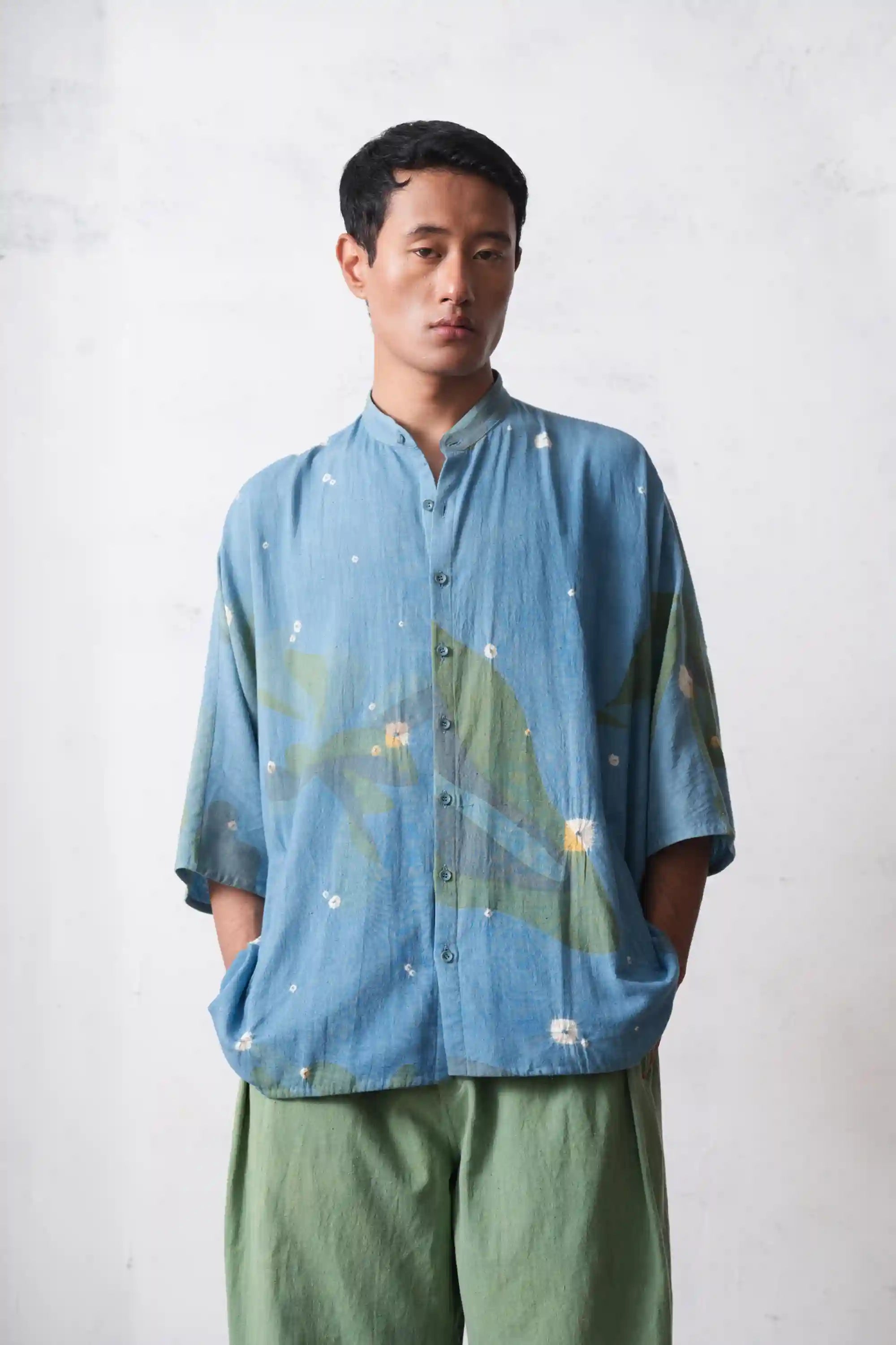Person wearing a blue floral shirt and beige shorts against a plain background