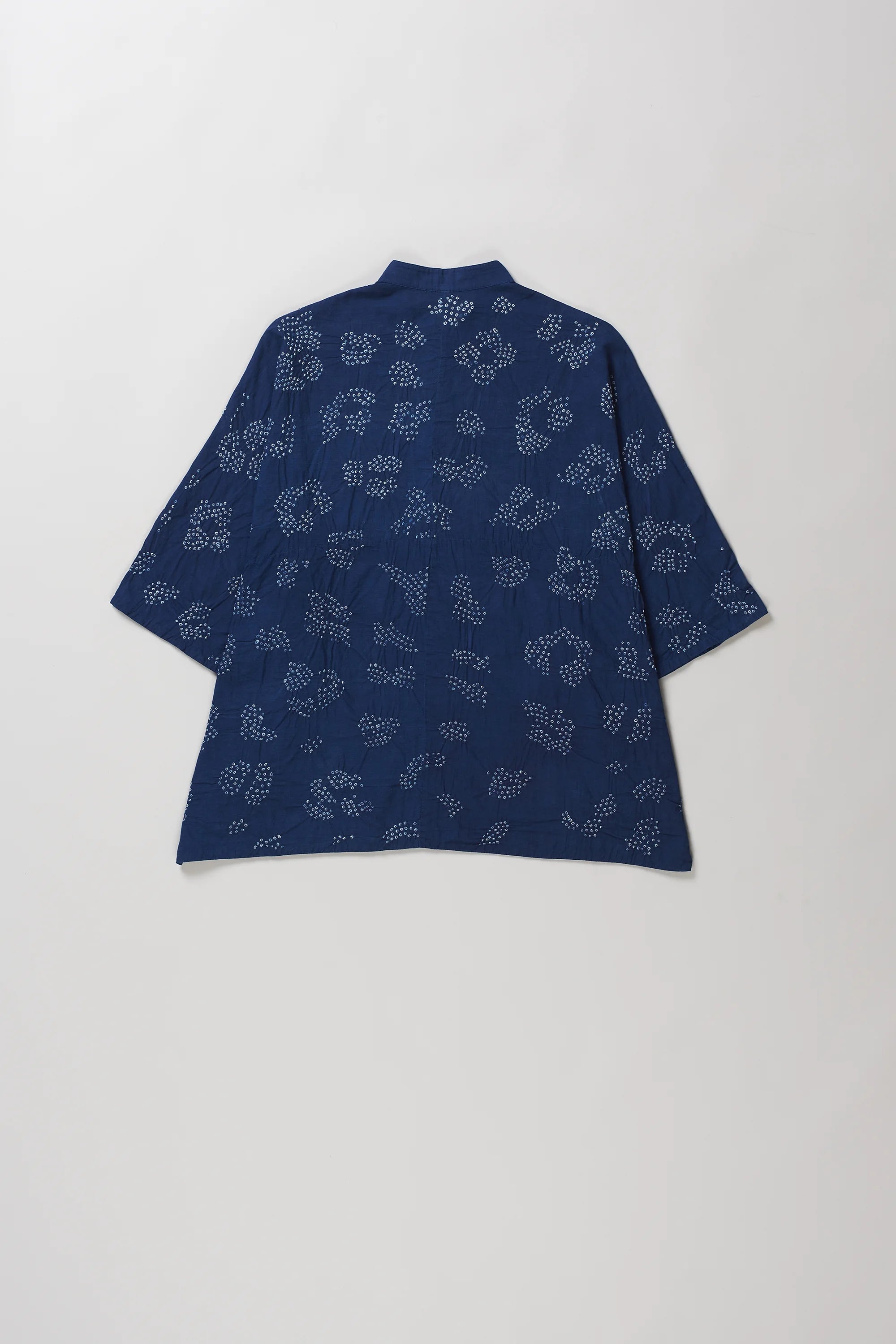 Back shot of indigo short-sleeve button-up shirt with bandhani, laid flat against a light grey background.