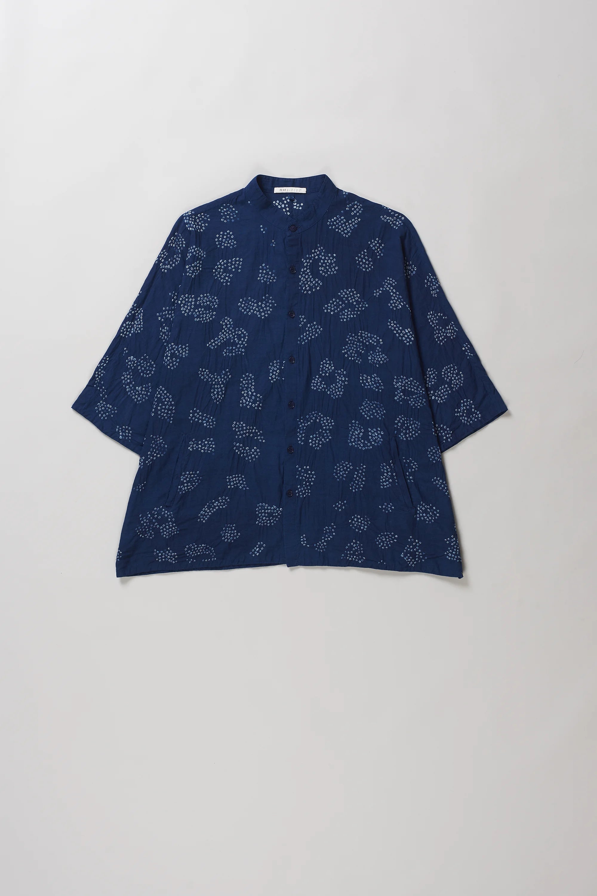 A indigo short-sleeve button-up shirt with bandhani, laid flat against a light grey background.