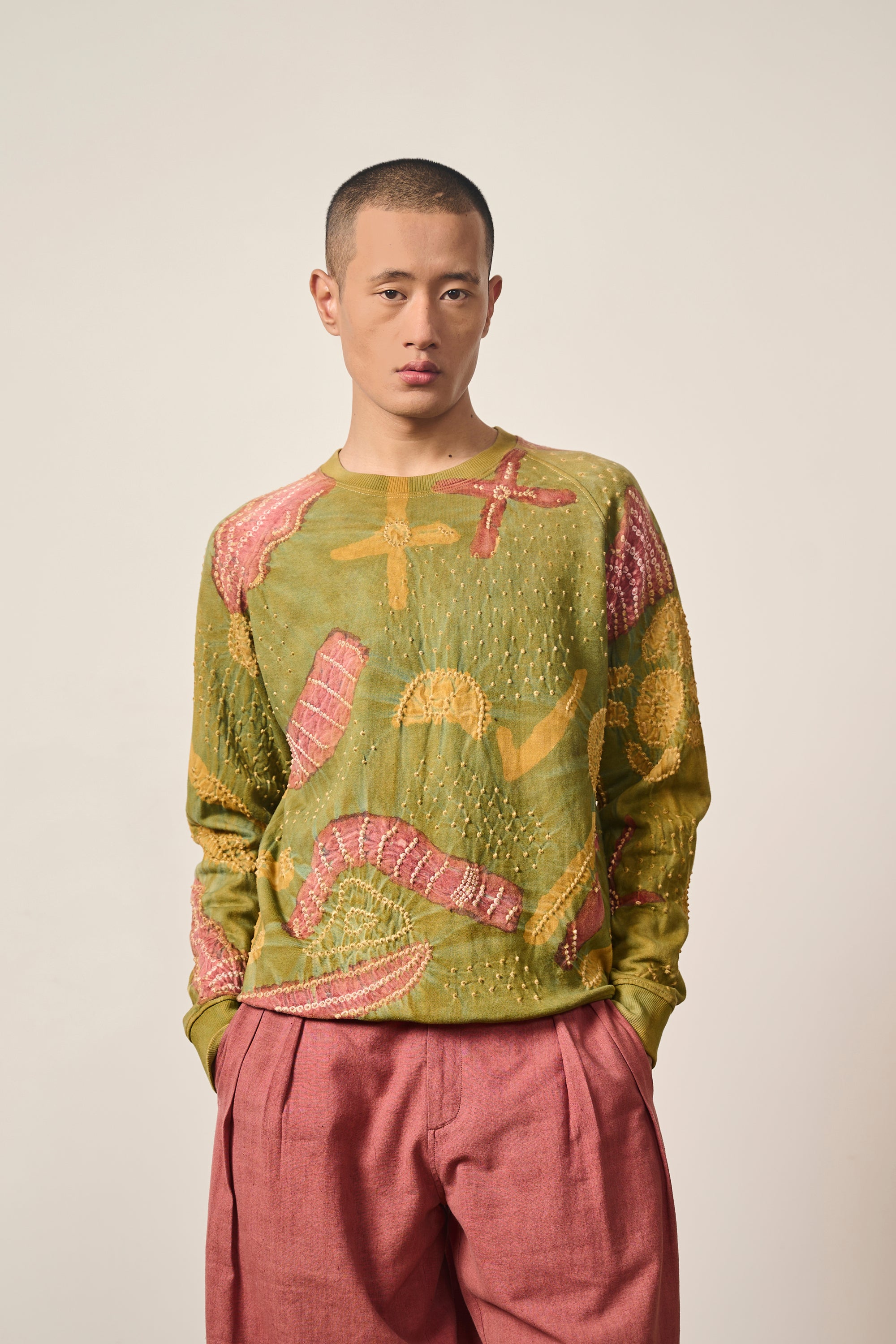 Man wearing a moss green patterned sweatshirt on a grey background