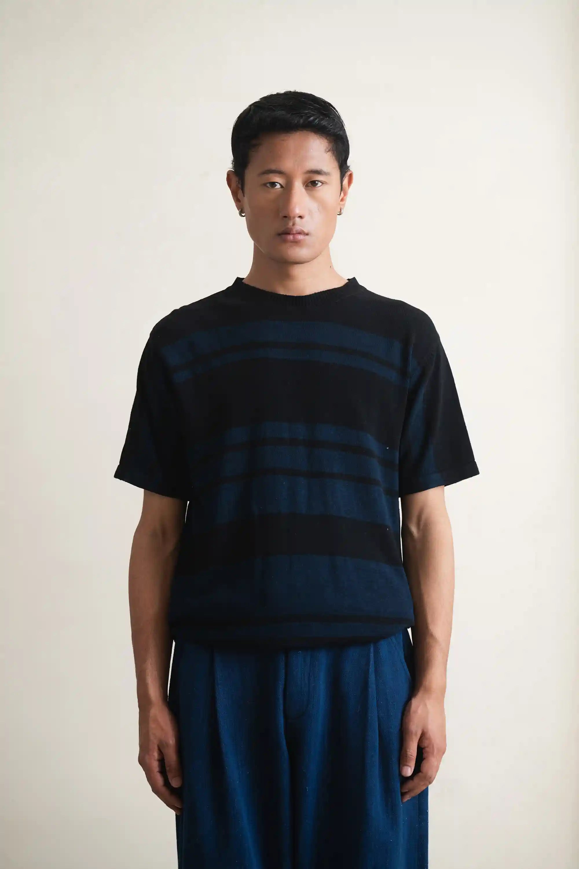 Person wearing a black and blue striped shirt with blue pants against a plain background