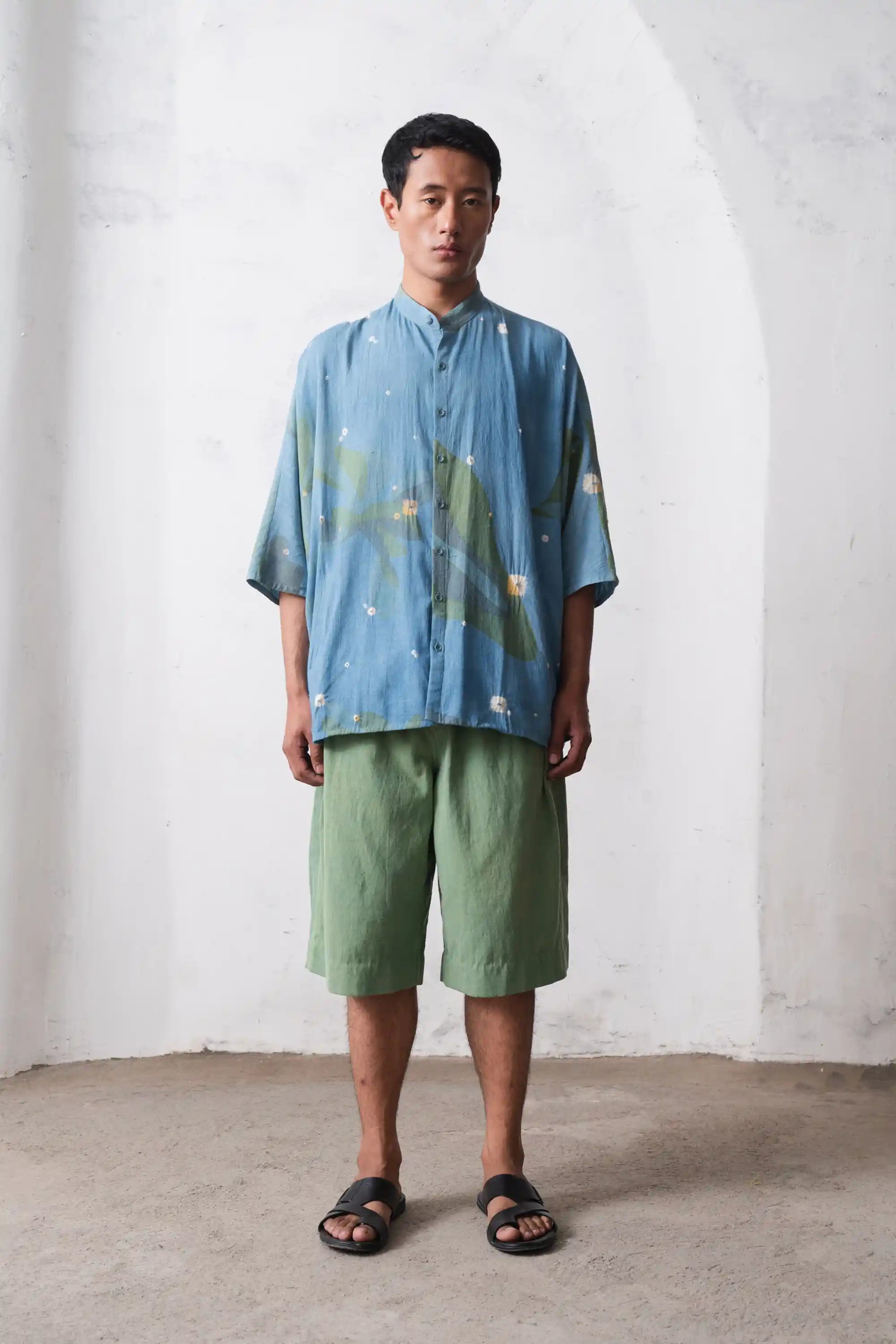 Man wearing a blue shirt and green shorts against a white wall.