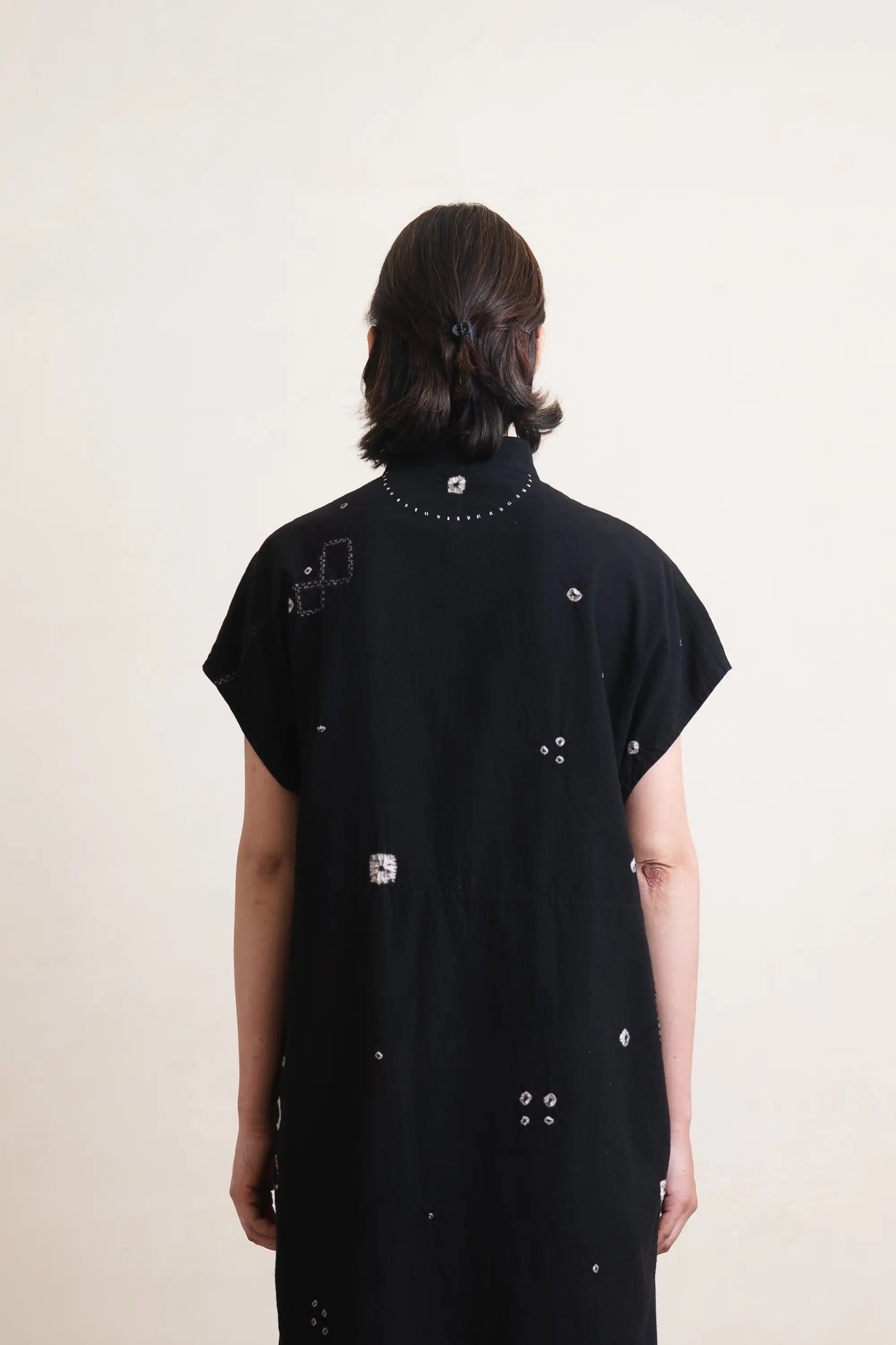 Person wearing a black dress with decorative elements on a plain background