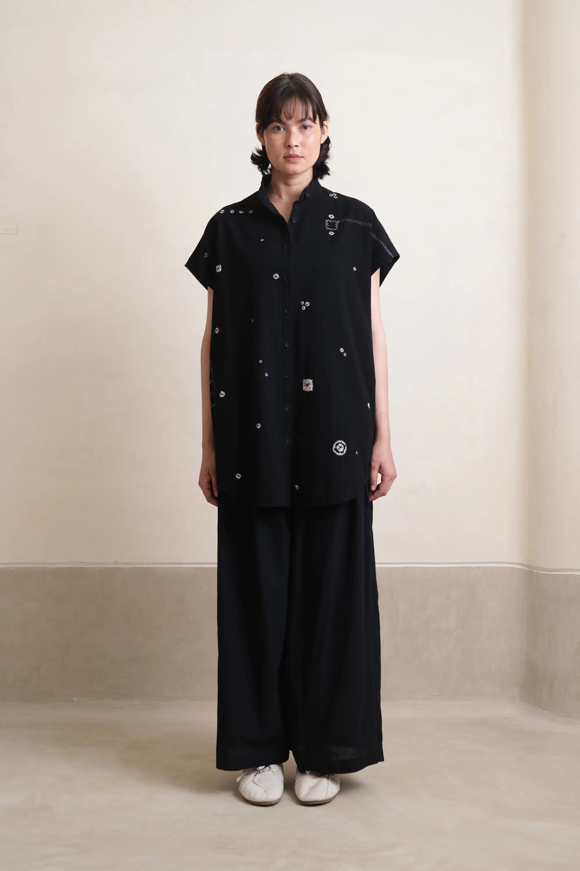 Person wearing a black outfit with white patterns against a plain background