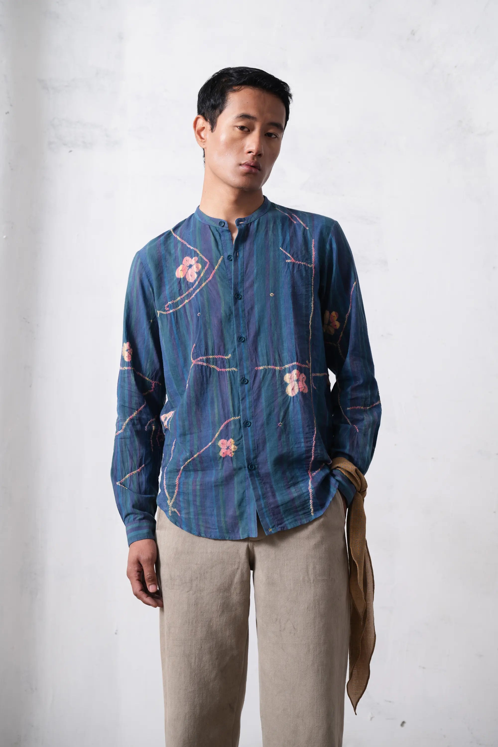 Man wearing a blue shibori shirt with beige pants against a light grey background