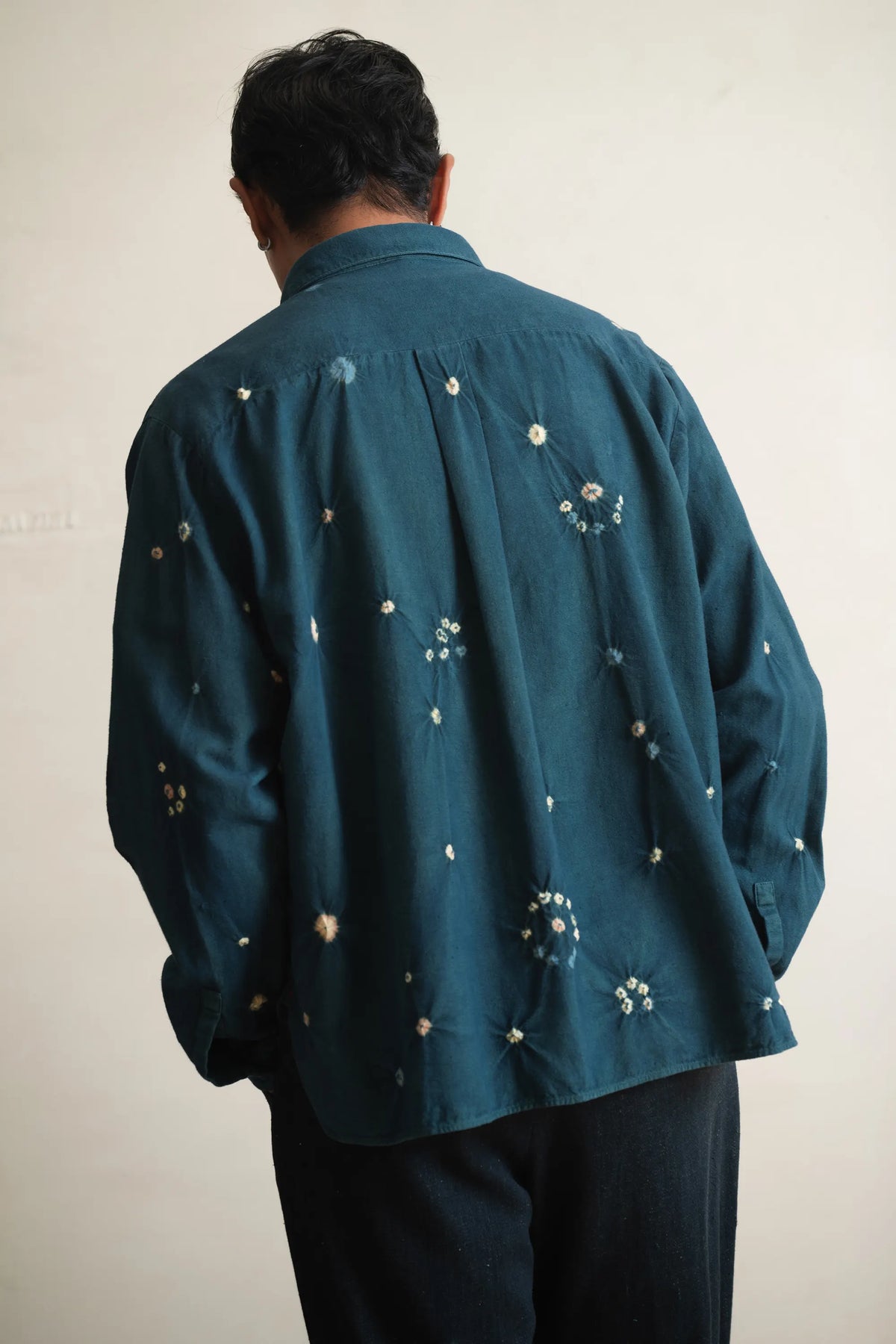 A back shot of a person wearing a bottle green shirt with bandhani on a light grey background